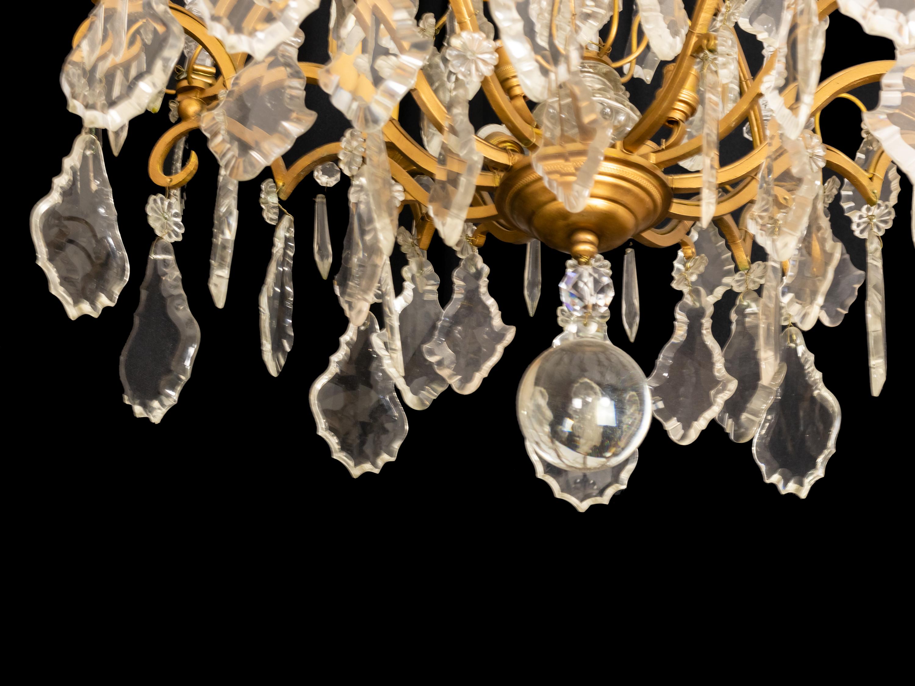 A Classic Louis XV style chandelier having 8 arms and 12 lamps (4 central).
The gilt metal frame is heavily laden with various sized crystal plaquettes.

Originally candle lit but now completely electrified.
Electric Installation reviewed recently