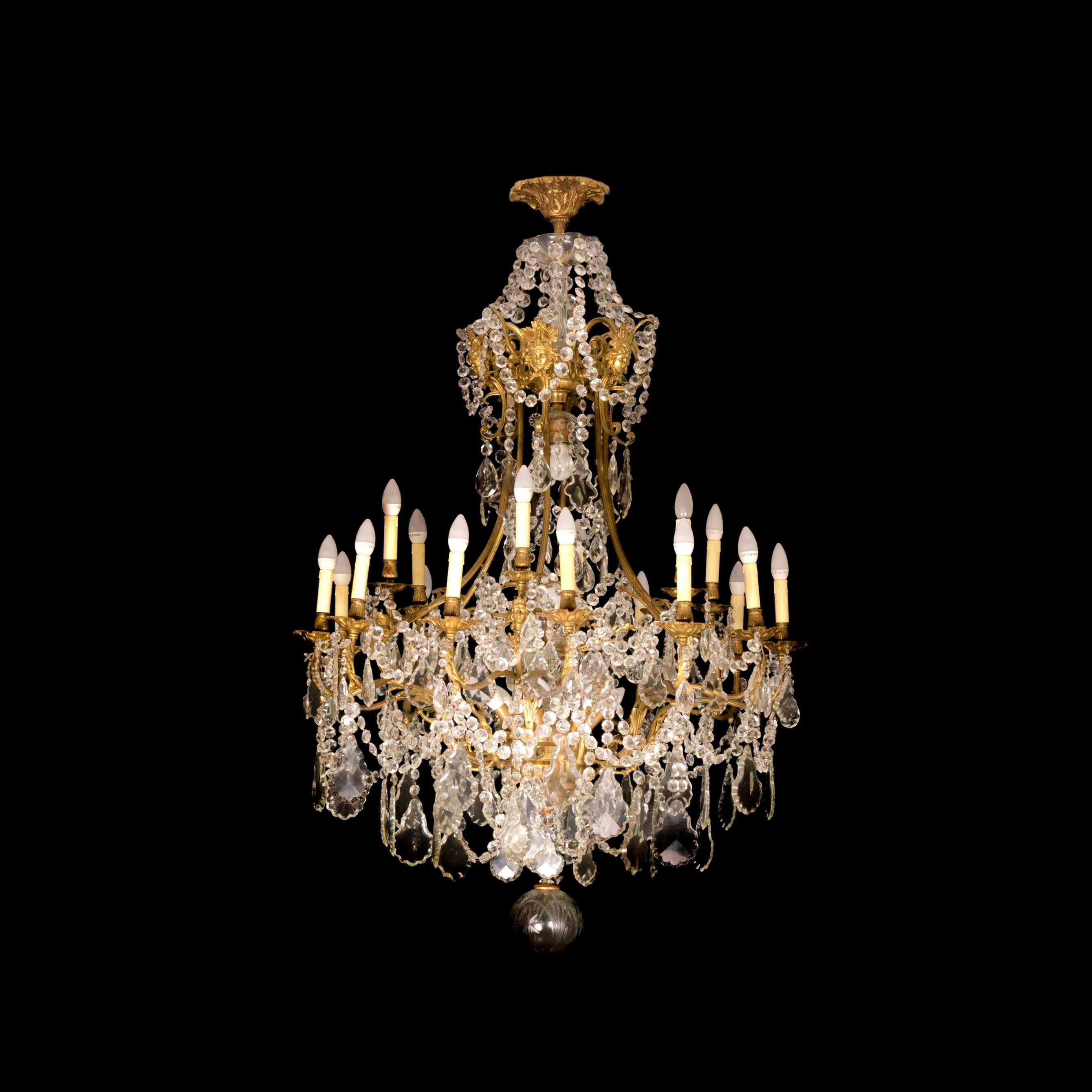 A Classic Louis XV style chandelier having 6 arms and 26 lamps (18 in the arms, 6 below, 1 central light, 1 on the top).

The gilt metal frame is heavily laden with various sized crystal plaquettes. 

Decorated with rare Gilt Versaille Bronze Style