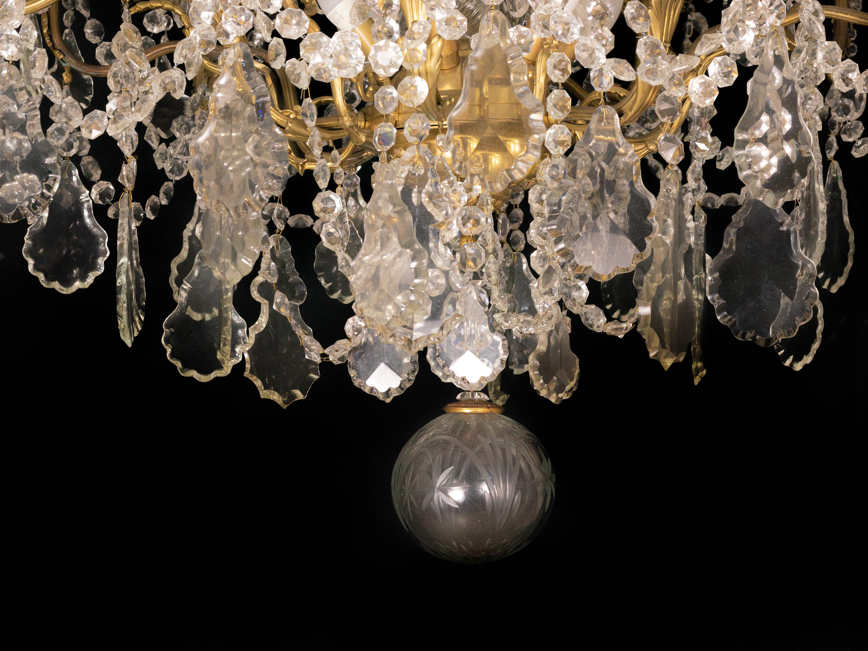 A Classic Louis XV style chandelier having 6 arms and 26 lamps (18 in the arms, 6 below, 1 central light, 1 on the top).

The gilt metal frame is heavily laden with various sized crystal plaquettes. 

Decorated with rare Gilt Versaille Bronze Style
