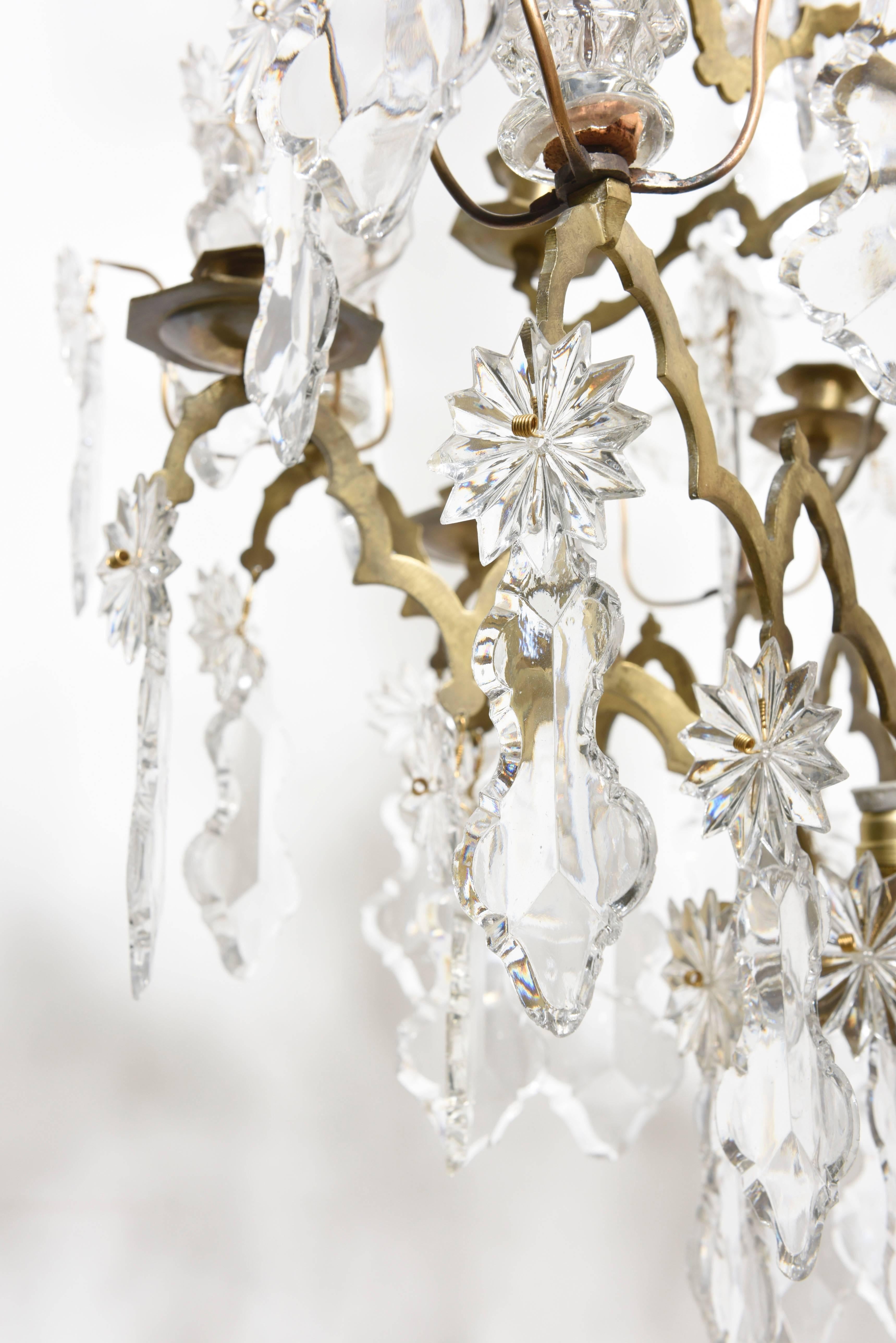 Grand lustre Louis XV en bronze doré et cristal à douze branches avec cristaux taillés, plaques, rosettes et gouttes à facettes. La tige étonnante et élégante s'élève vers une gerbe de fleurs et de cascades qui retombent en cascade avec des éclats