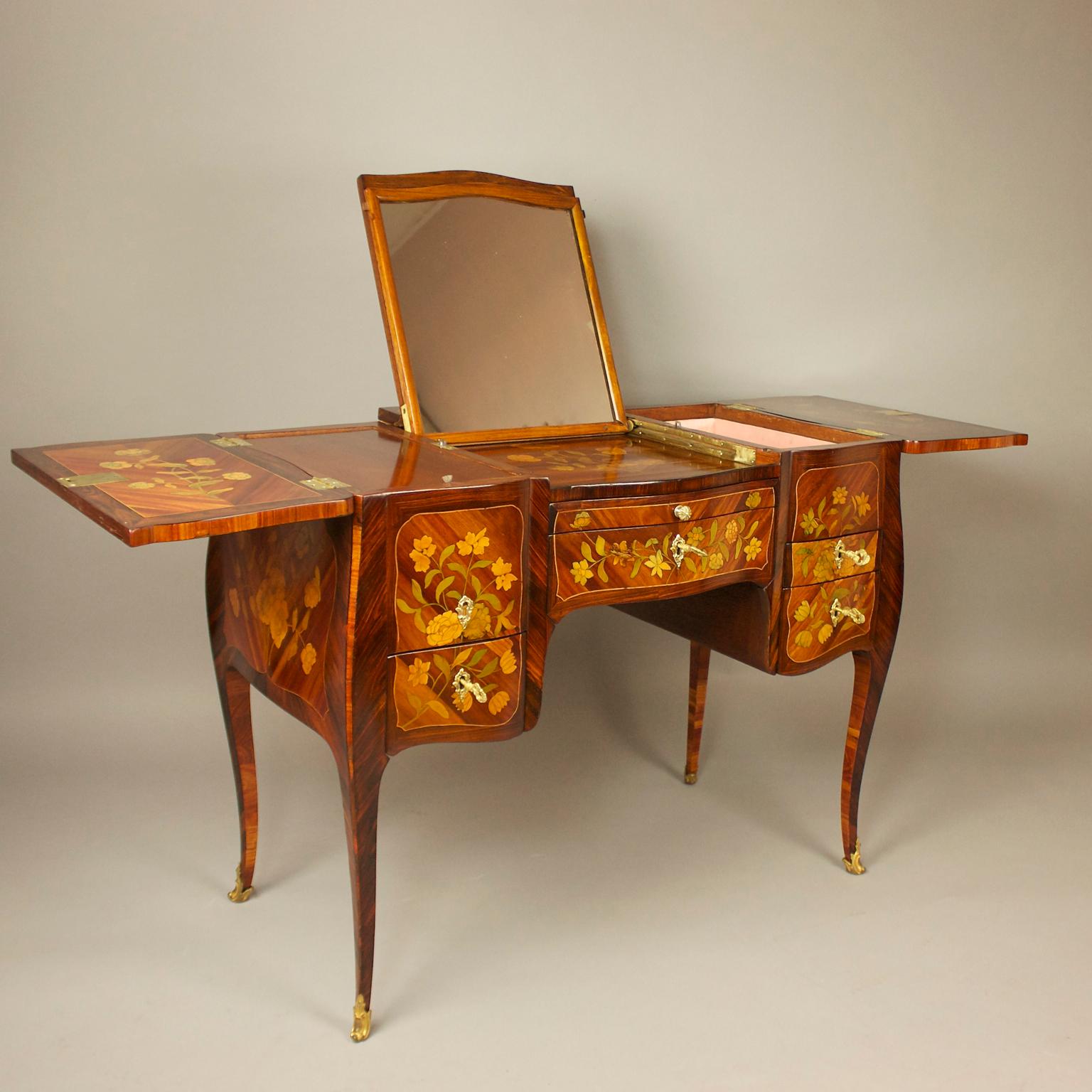 A Louis XV marquetry dressing table or 'perruquiere' attributed to Pierre Roussel (1723-1782). The table is veneered in tulipwood and other woods, forming floral marquetry panels with a the top central panel incorporating a trophy of finely inlaid