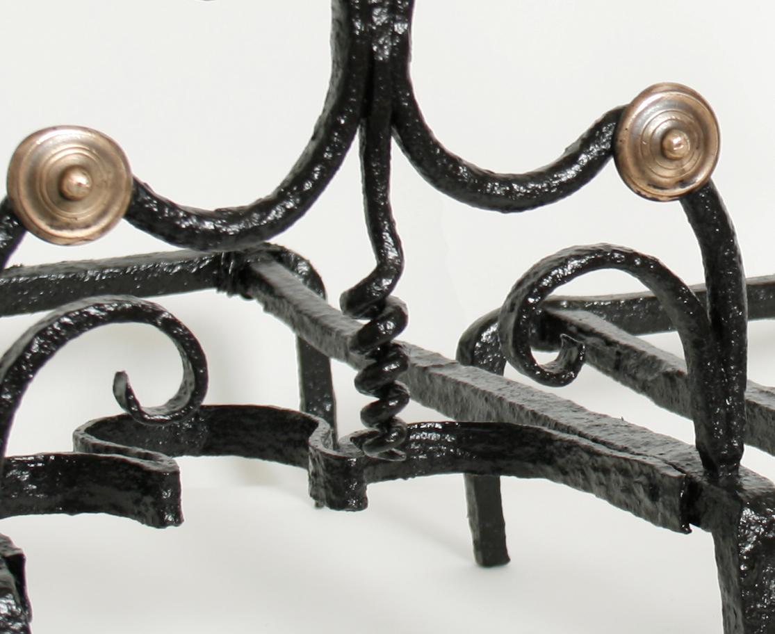 These exceptional andirons are made of forged iron and have cast brass finials and button mounts. The beds are wide and easily hold large or small logs. They have a scrolled profile with a coiled screw centre stem topped by a hexagonal cast finial.