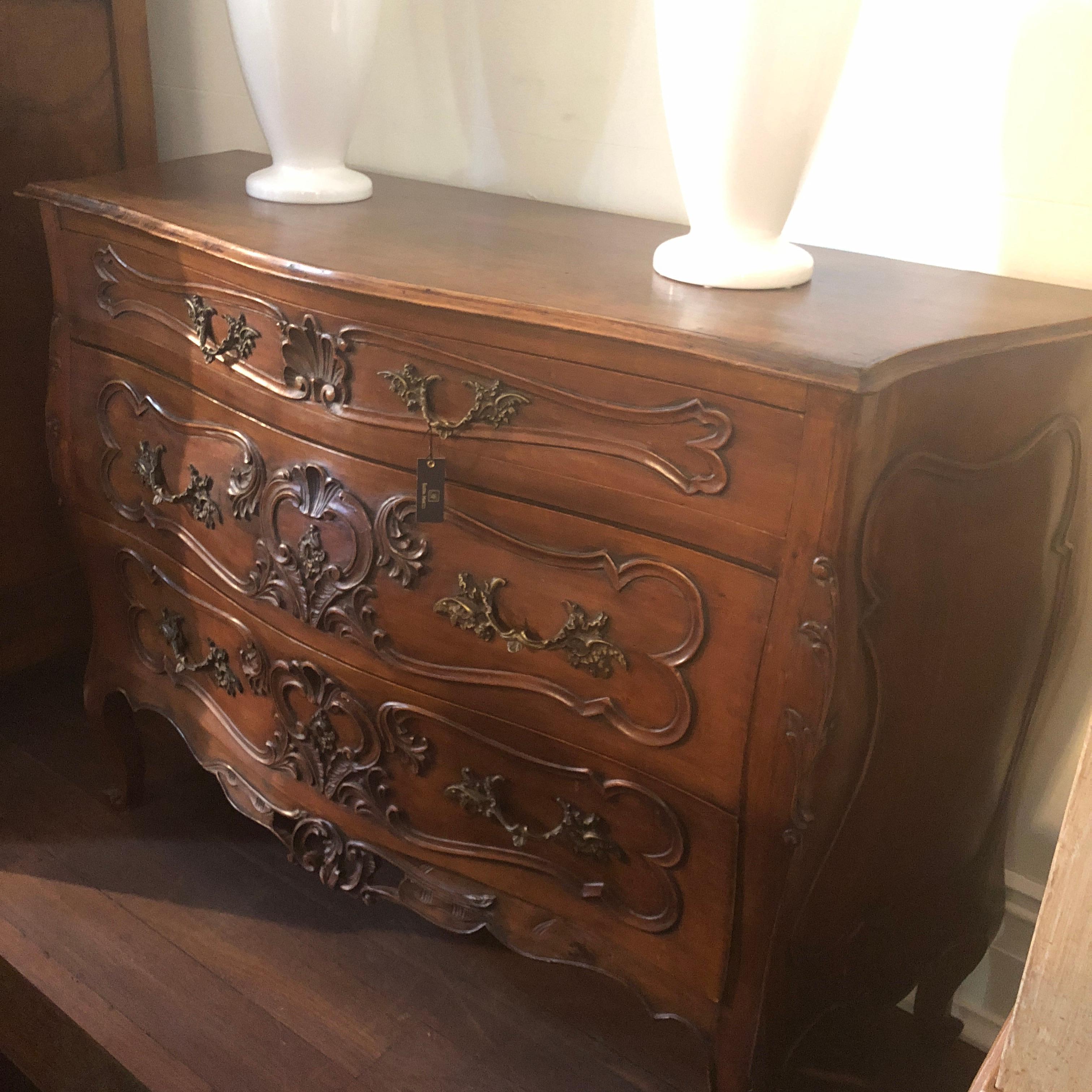 Stunning, ornate Louis XV carvings adorn this beautiful walnut commode, accompanied with cabriole legs and the classical, 'bombe' shape. The original brass French lock remains with this piece along with ornate brass drawer pulls. This rich walnut