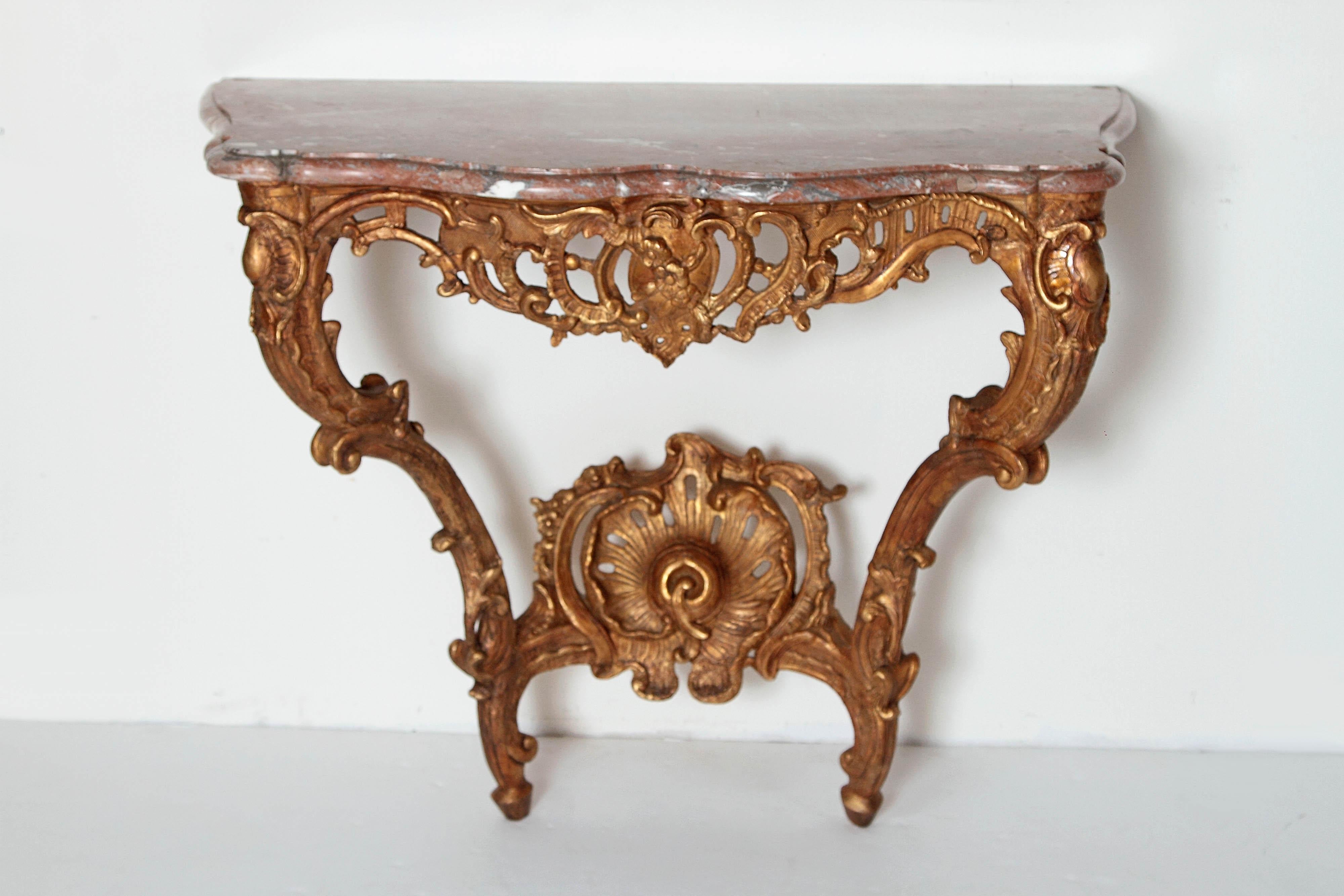 A beautiful Louis XV French 18th century giltwood console table with marble top. Heavily carved and pierced front apron. Two carved front legs curving into a carved shell motif. The top is the original rose colored marble. 18th century France.