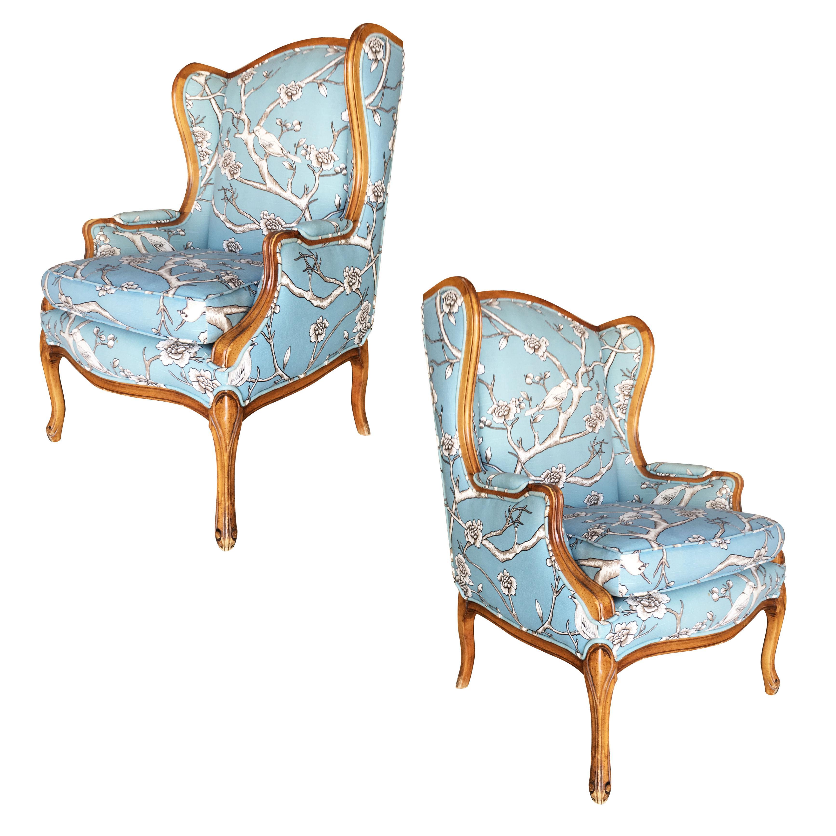 Vintage pair of French Country inspired walnut wing back lounge chairs. The chairs feature a hand carved frame with blue floral fabric upholstery, circa 1950.