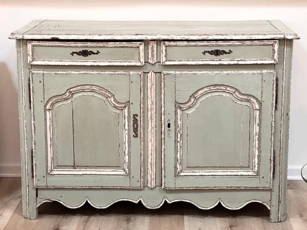 French Provincial carved wooden buffet, 18th/19th Century, in the provincial Louis XV taste, having a distressed green-blue-gray painted finish with cream details, two drawers above double doors, scalloped apron, and rising on curved legs.   h.