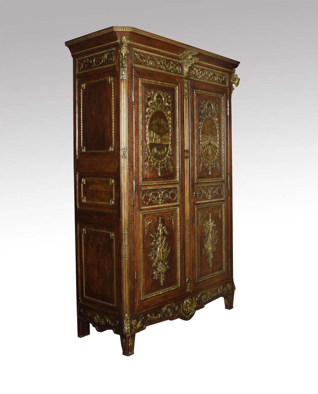 Louis XV French walnut armoire, the projecting cornice surmounted with carved ram’s heads, above two large paneled doors with detailed gilded scenes incorporating baskets of flowers and trailing festoons, with architectural vistas and musical
