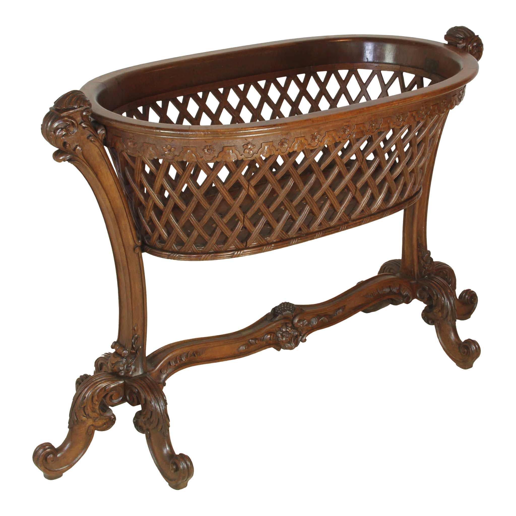 This delicately carved, walnut cradle features an oval, lattice basket supported by bowed posts terminating in tripod feet. The feet begin with acanthus leaves and end in decorative scrolls. The tripods are united by a stretcher, which is carved