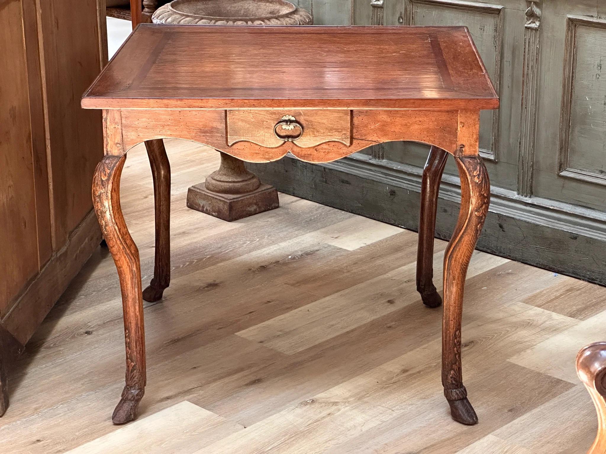 Louis XV Games table with banded top and one drawer; the legs carved with foliage, on hoof feet.  The top possibly later or reconfigured.  The base 18th Century.  26.5” h. x 30 “ x 28.5
