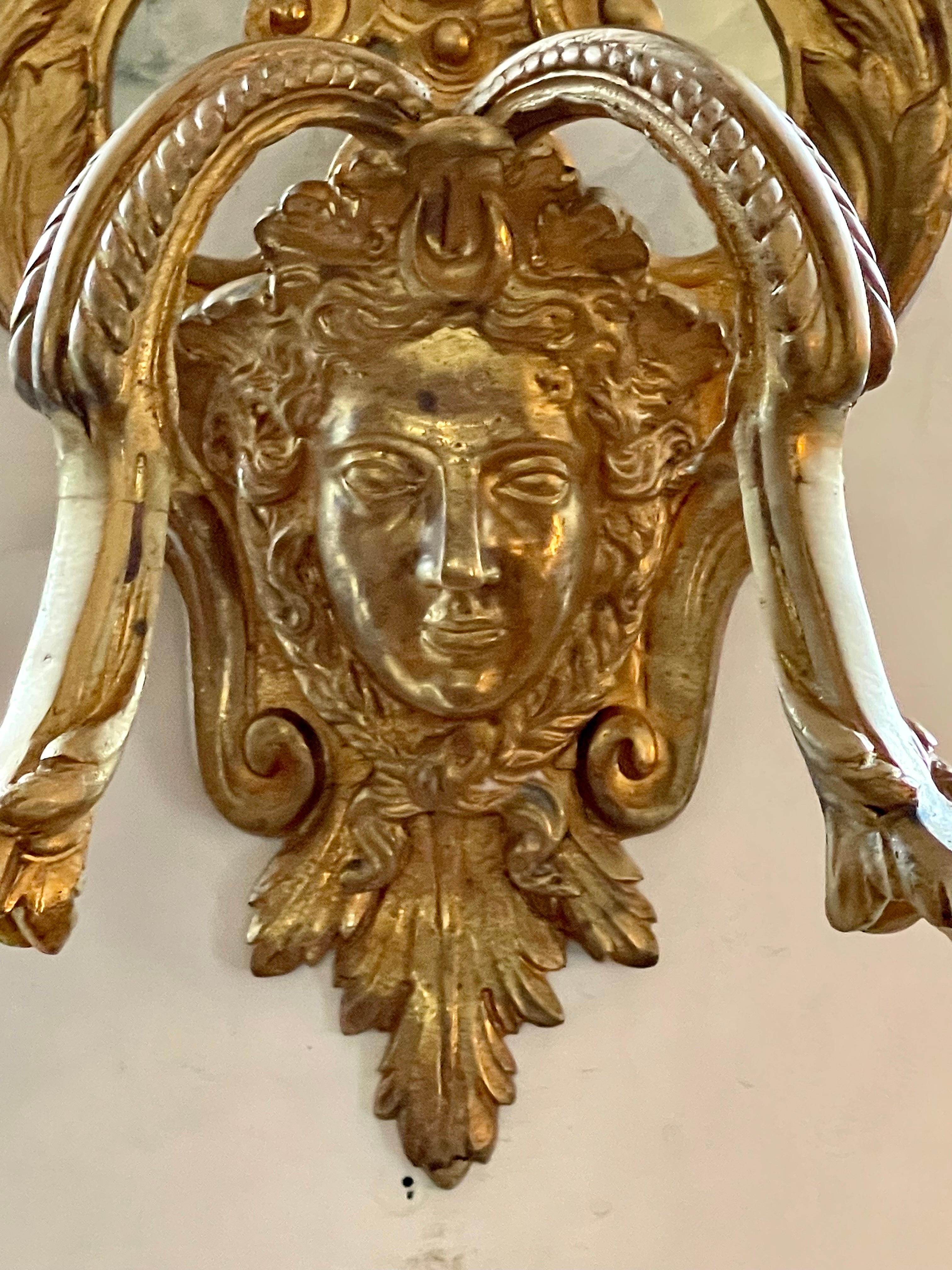 A Fine Pair of French Louis XV style gilt Bronze double arm Wall sconces. Two arms decorated with feathers and bellflowers rise out of the faces of caryatids. The Lair shaped Backplate is decorated with garlands, foliate designs, and shells, topped