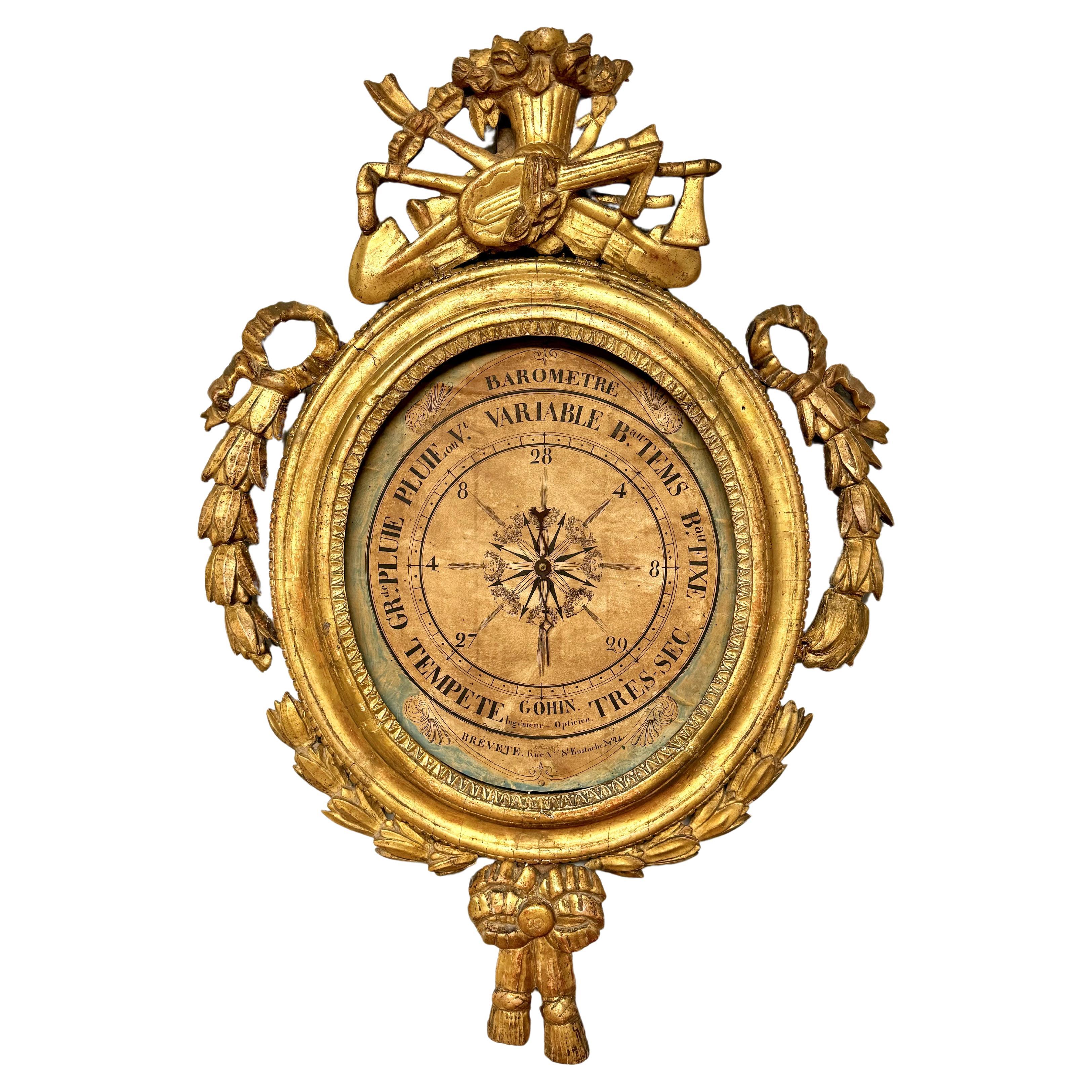 Louis XV French Barometer by GOHIN in giltwood in an oval shape. Features carved and gilded wood with ornamentation of tools, cascading foliage and bows. Original background displays French writing describing weather conditions. A lovely piece for