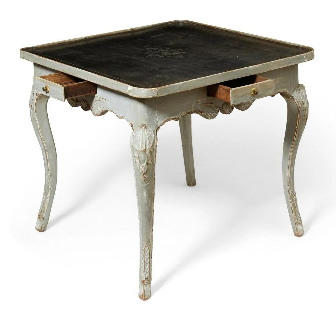 Louis XV grey painted games / card table with black leather playing surface with embossed / tooled center decoration and border, four (4) small drawers, one (1) on each side for each player, placed in the center of the shaped apron, carved cabriole