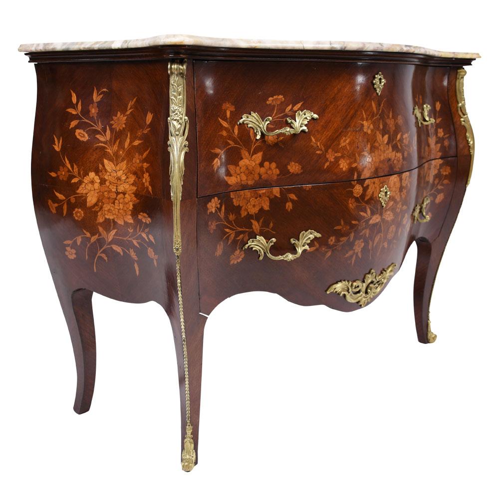 This 1950s French Louis XV-style commode or chest of drawers is made of solid wood finished in a beautiful mahogany color stain with intricate floral motif marquetry designs. The chest features top of the commode features a multi-colored marble top,