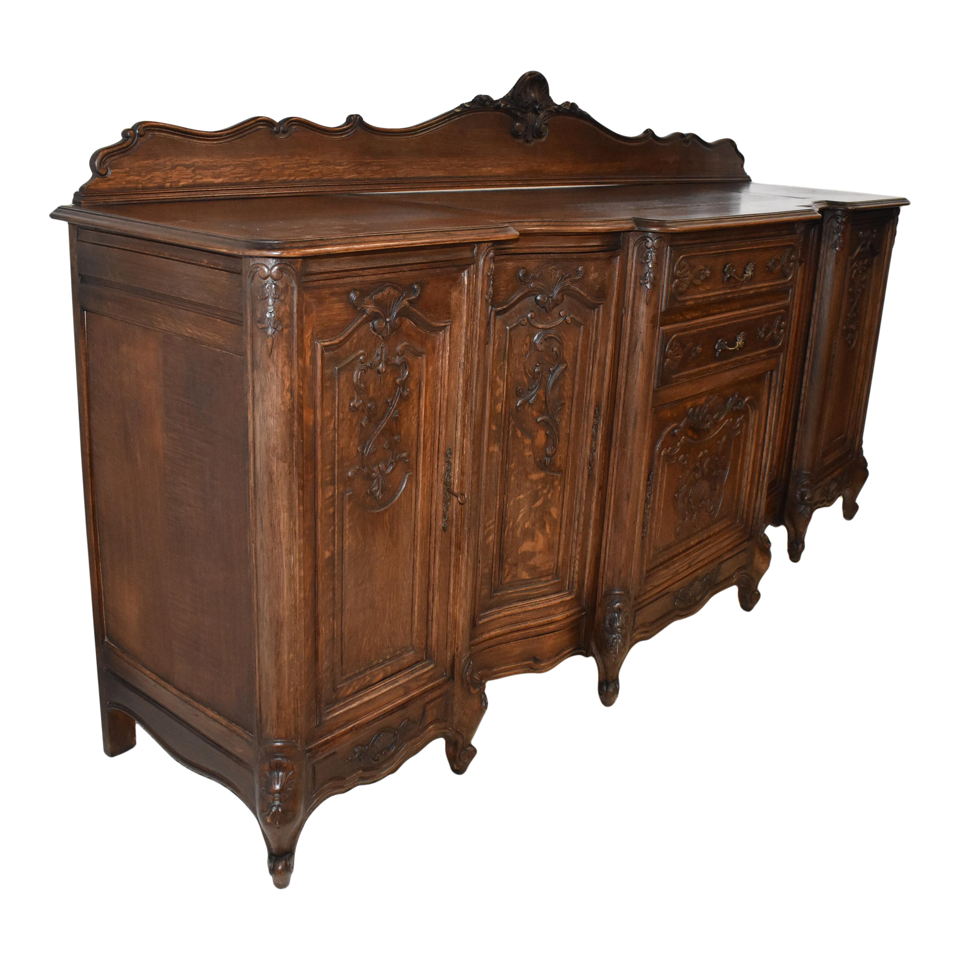 Crafted from solid European oak and finished with a medium stain that enhances the beauty of the wood's grain, this gorgeous sideboard from the early 20th century features carvings of shells, acanthus leaves, flowers, and scrolled lines consistent