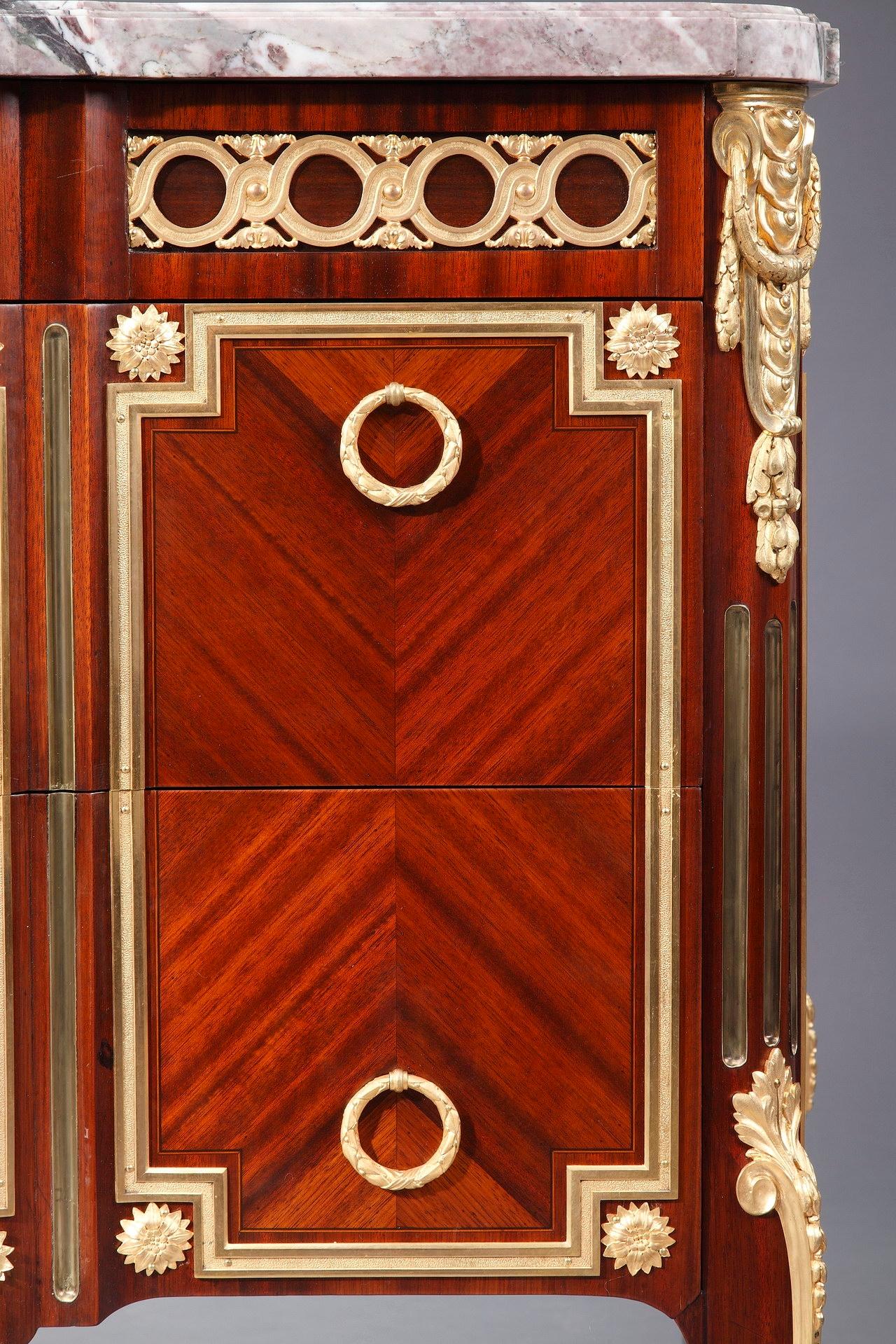 This Louis XV-Louis XVI Transition style commode, crafted of intricate parquetry veneer, displays the mastery of the famous 19th and 20th century maître ébéniste Mercier Frères. The compact form holds two large drawers and the belt, one smaller