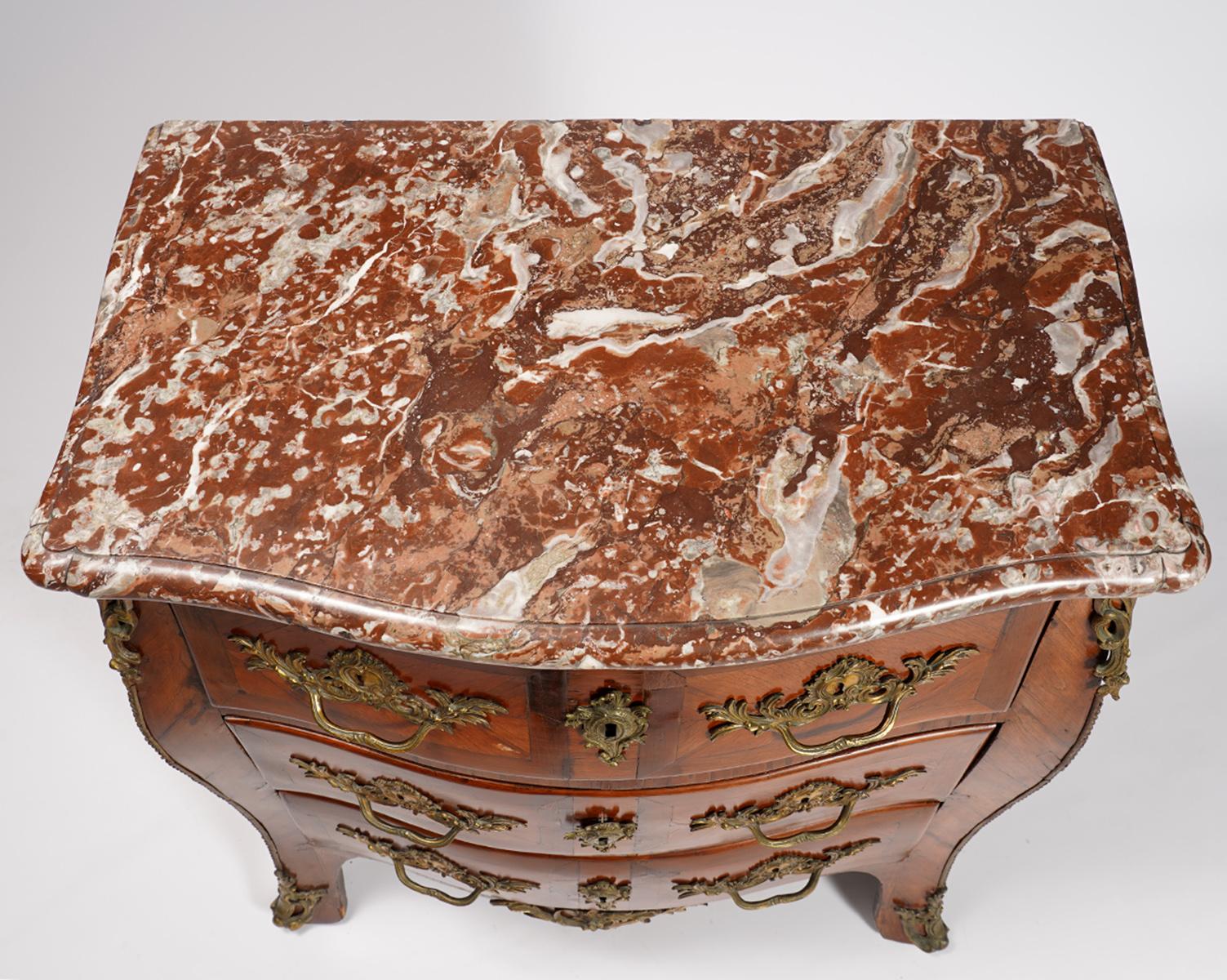 This period small size Louis XV serpentine front commode, dating to circa 1765, features a shaped and molded marble top above three parquetry kingwood and tulipwood drawers mounted with original Rococo bronze handles and escutcheons flanked by