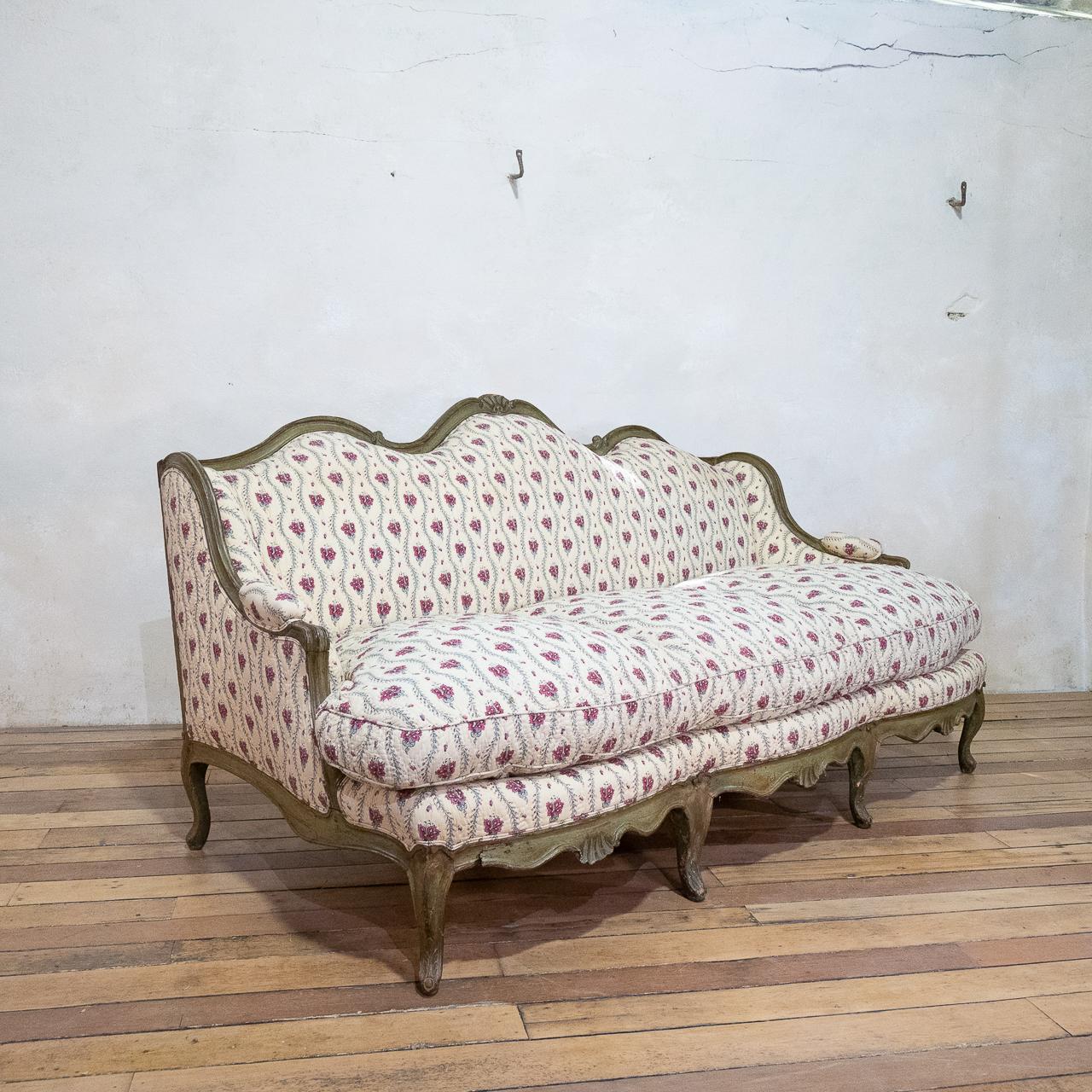 A Louis XV period Canapé à Oreilles serpentine-shaped sofa. Featuring carved detailing, decorated with floral motifs and acanthus, with original Verde paint. The seat rails display central scallop shell carved motifs raised on cabriole legs headed
