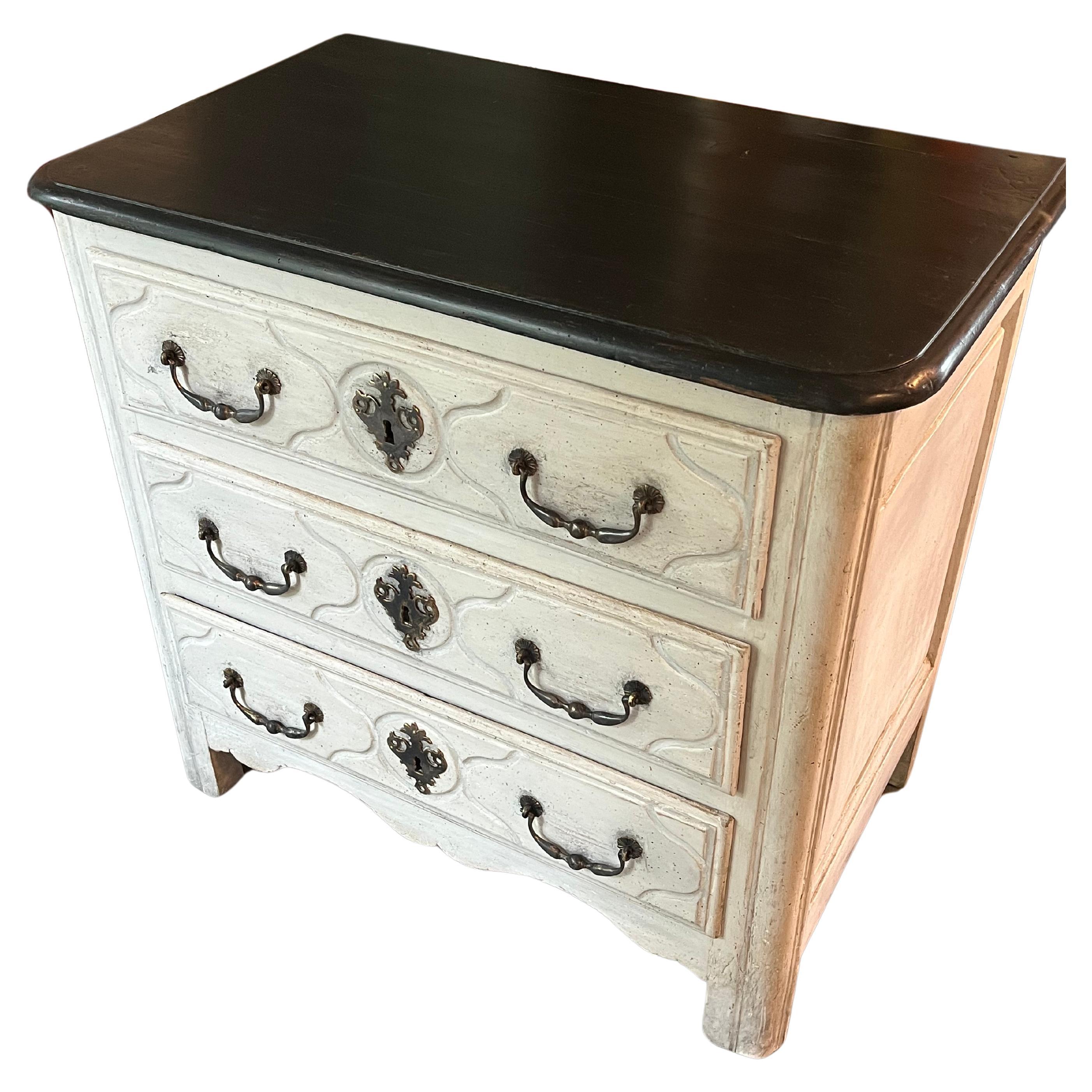 Un'affascinante e rara petite commode del XVIII secolo, periodo Luigi XV. Il piano conforme in legno ebanizzato sovrasta 3 cassetti intagliati con ferramenta in bronzo patinato, conservando le serrature originali. Finitura verniciata color crema con