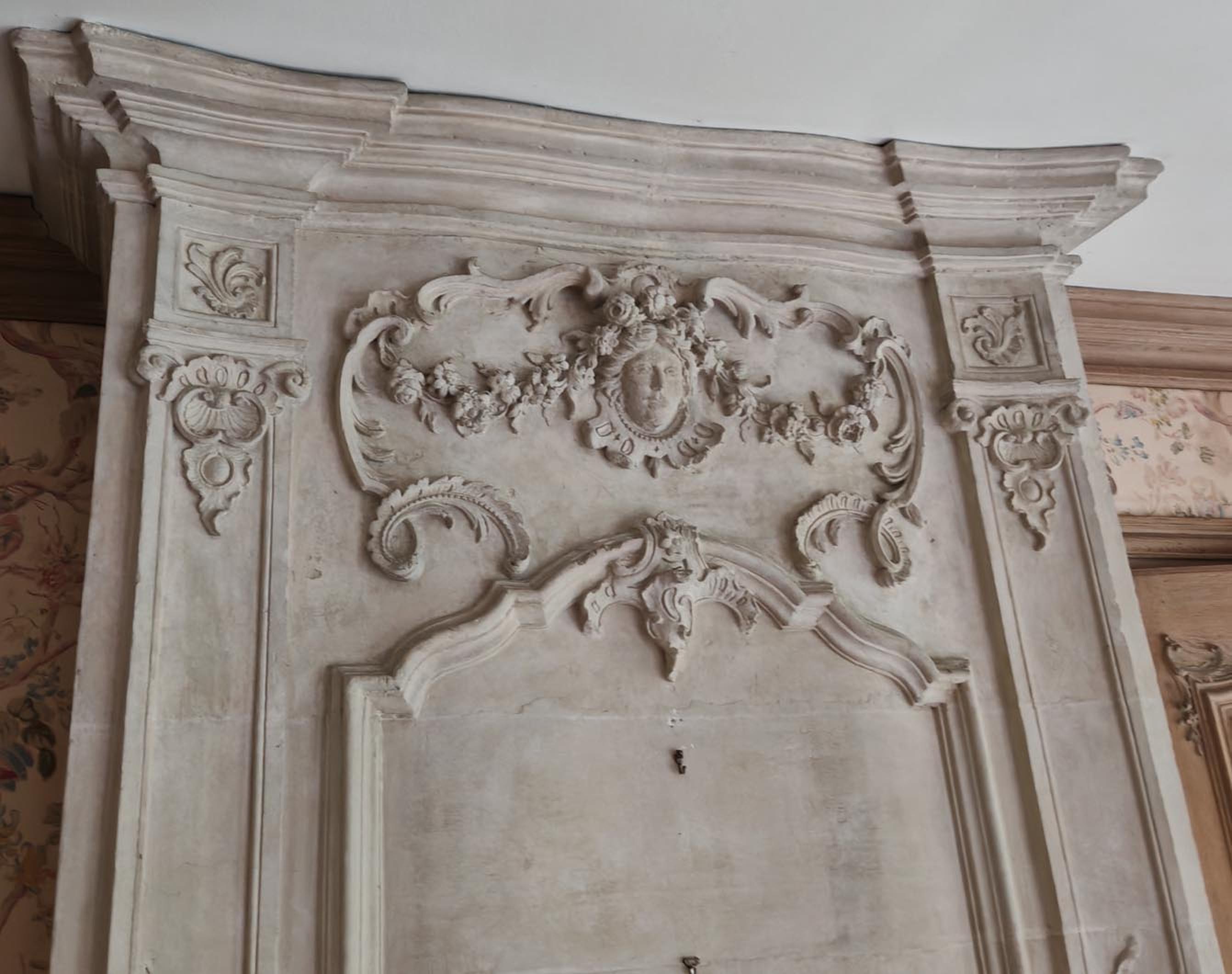 Cette cheminée en pierre d'époque Louis XV se distingue par la richesse de son décor, empruntant au vocabulaire ornemental du style Rocaille. Le trumeau de la cheminée est également très élaboré, une caractéristique baroque.

La partie inférieure du