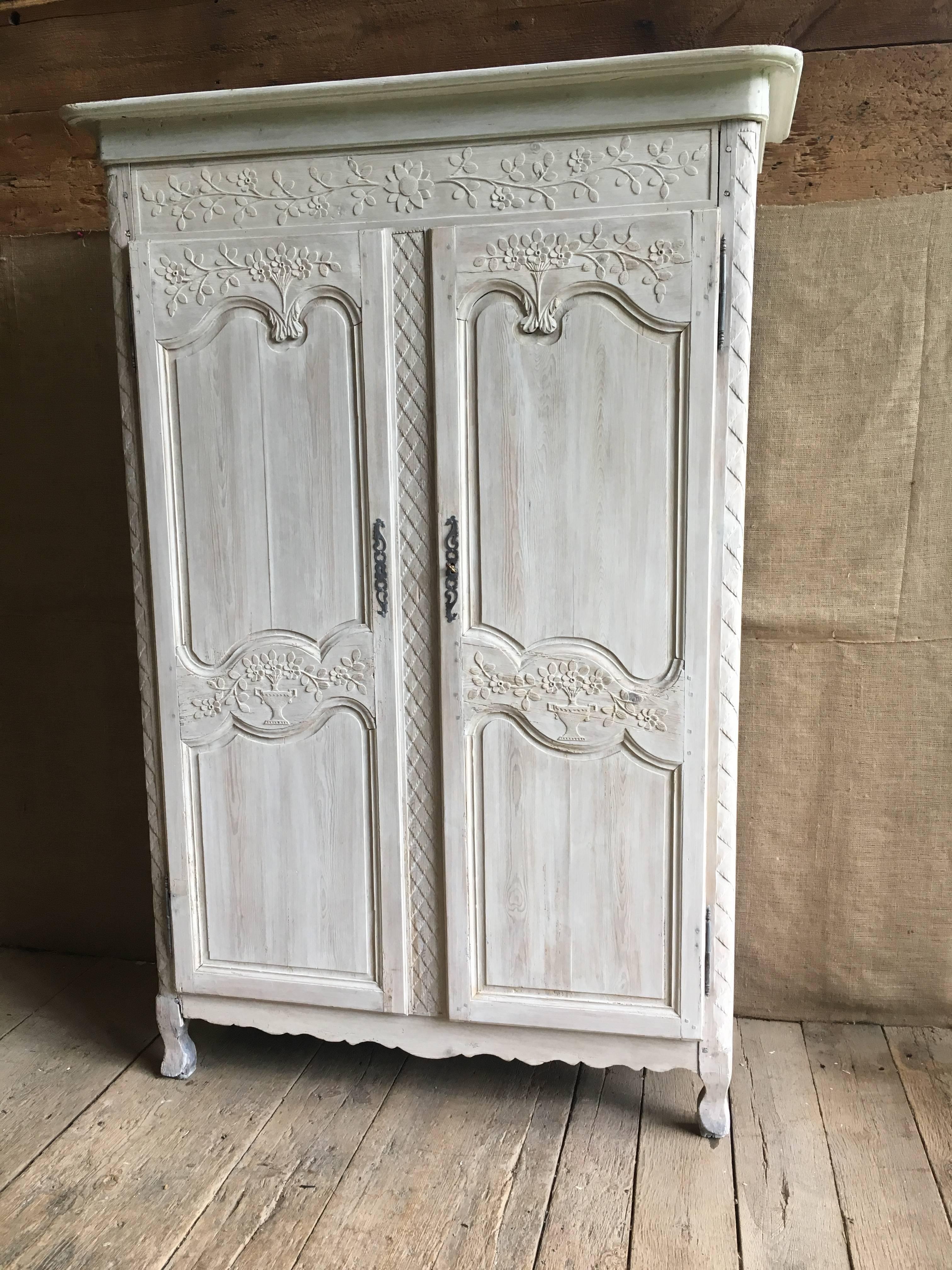 A French Louis XV period pine armoire from Normandy, circa 1780, abundantly carved with bouquets, baskets, garlands, etc. and with a bleached and whitewashed finish. The interior has two shelves and is painted light blue/grey.
Dimensions at crown: