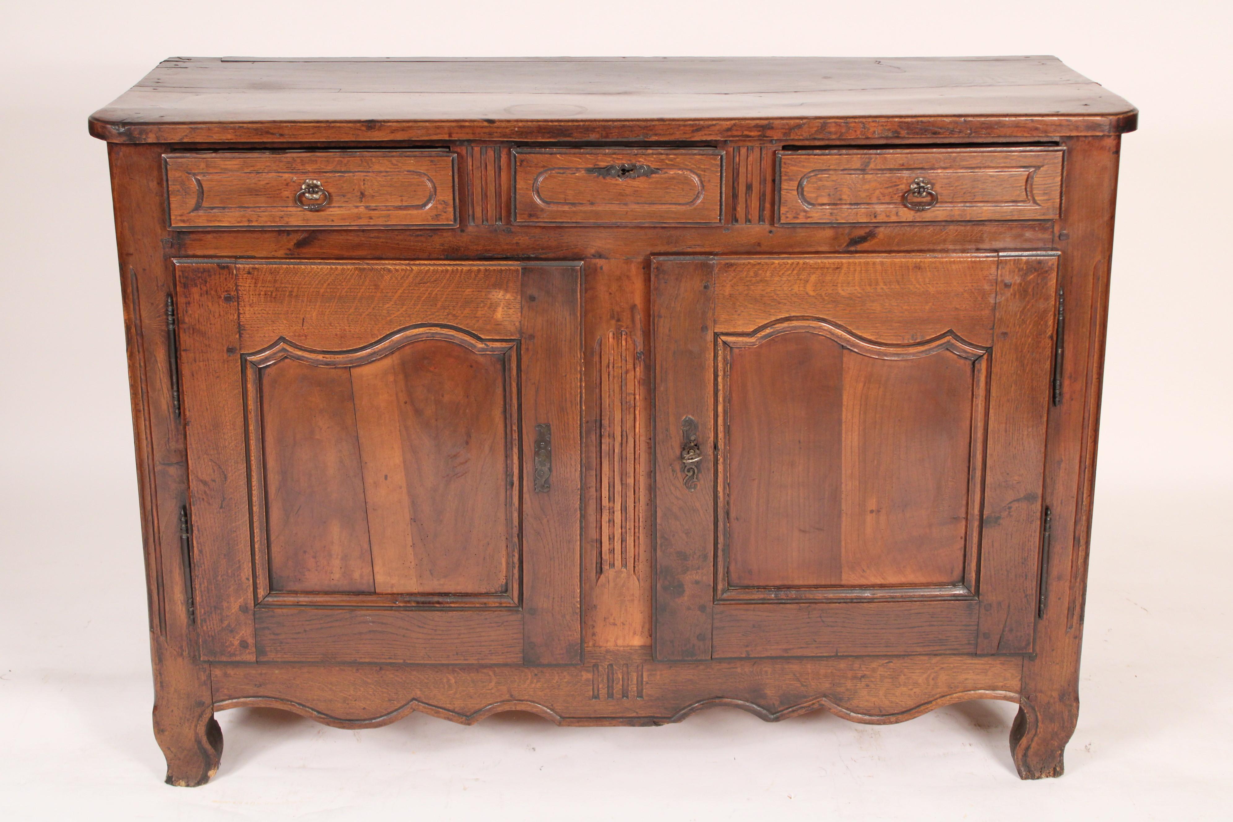 Antique Louis XV provincial style oak buffet, early 19th century. With a 3 board top with rounded corners, 3 drawers over two cupboard doors, a scalloped apron resting on slight cabriole. Nice old oak color, mortise, tenon and peg case construction
