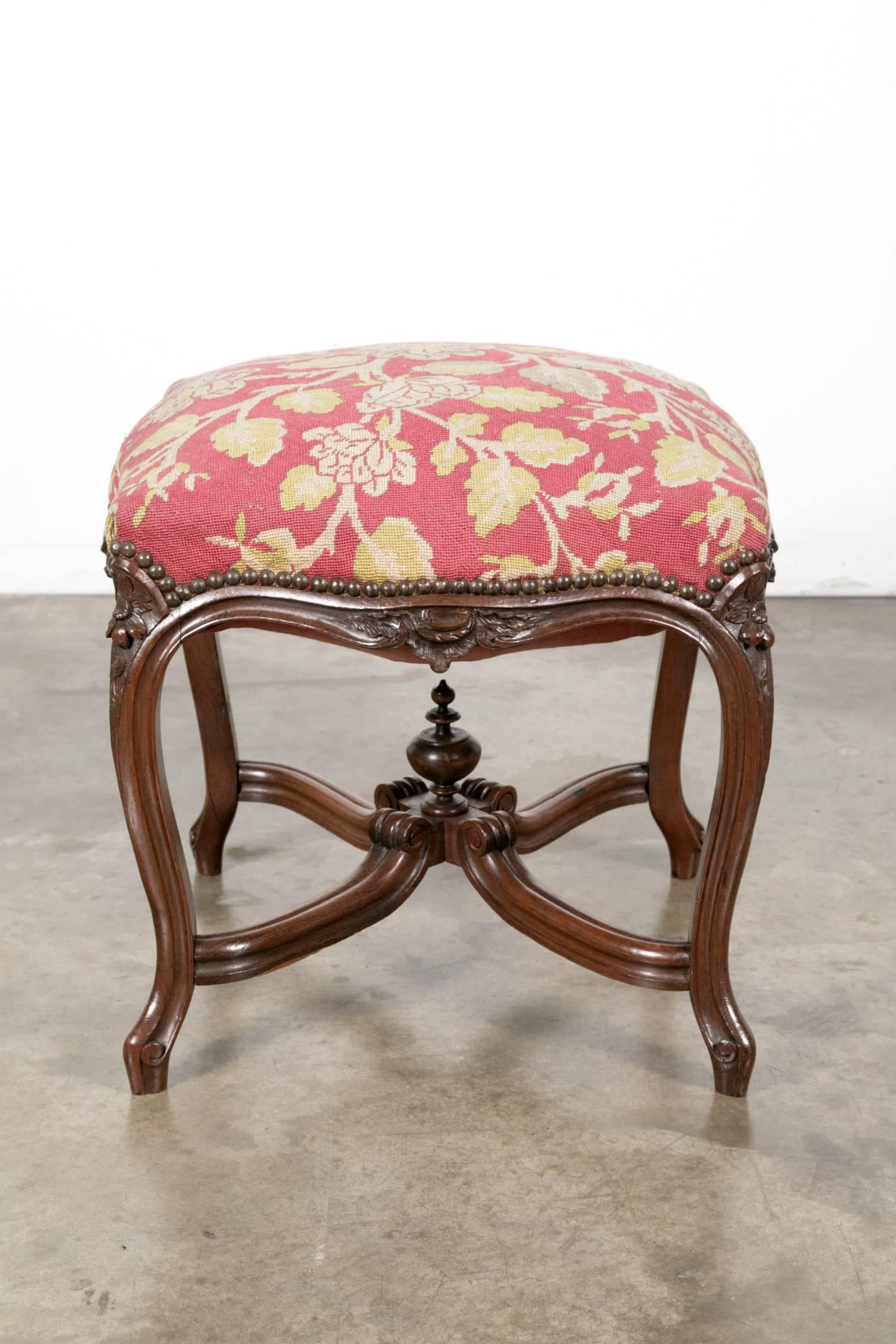 Add beautiful color to your living space with this ornately carved rosewood Louis XV style French court tabouret with finial mounted cross-stretchers from Lyon. Upholstered with the original handwoven floral needlepoint this footstool can be used to
