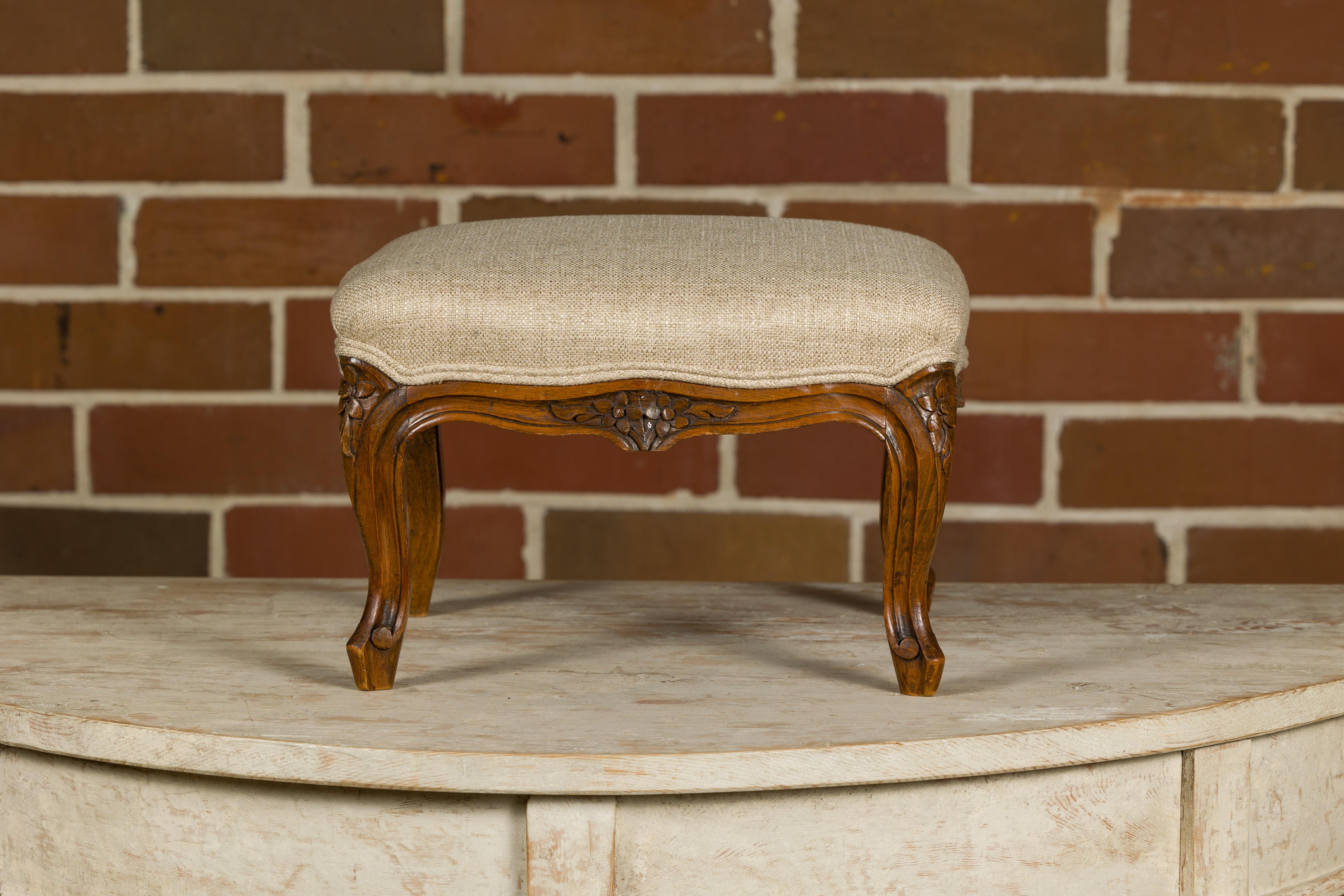 A French Louis XV style wooden footstool from the 19th century with carved cabriole legs and double welt linen custom upholstery. Elevate the elegance of your living space with this exquisite 19th-century French Louis XV style wooden footstool.