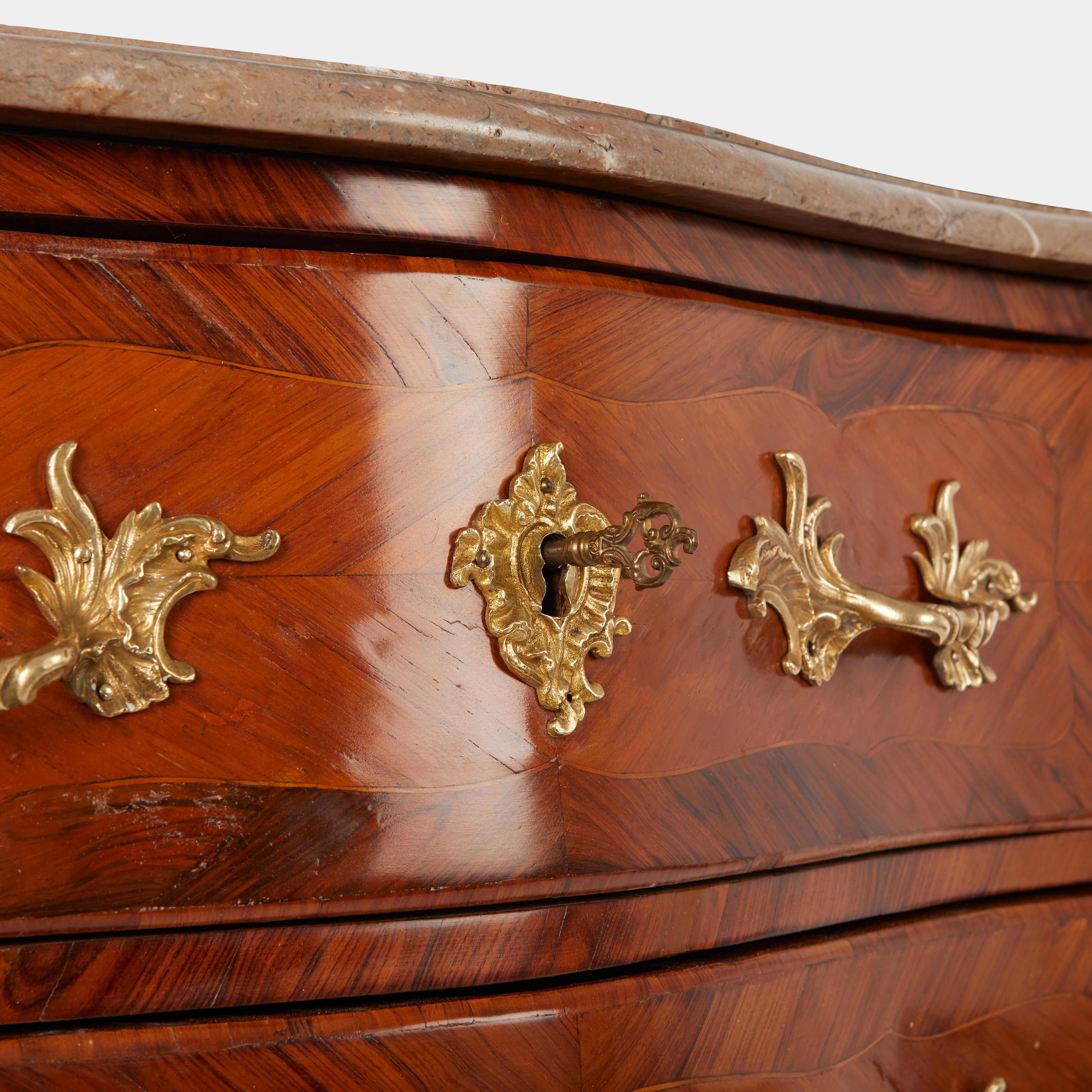 Commode française de style Louis XV à trois tiroirs, à façade et côtés façonnés, plaquée de noyer et de bois de rose. La carcasse en chêne est montée avec des poignées, des montures et des sabots moulés et ciselés, estampillés deux fois par le