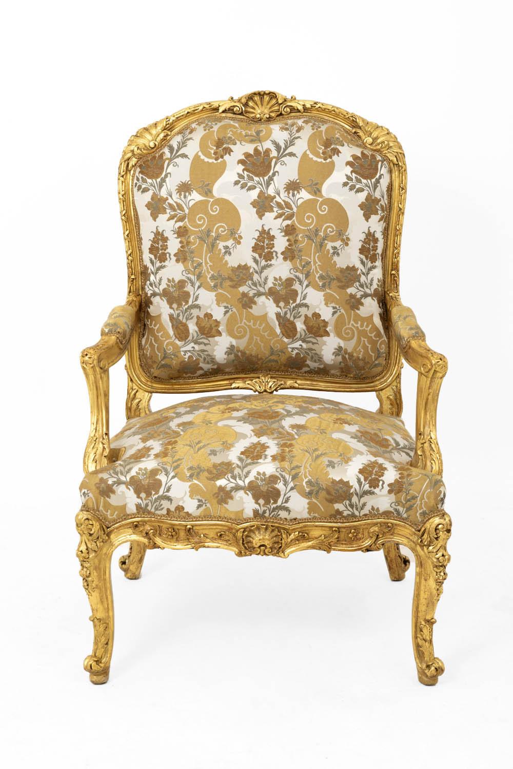 Louis XV style à la Reine armchair in giltwood standing on four cabriole legs with a decor of rocaille cartouche and acanthus leaves. Scalloped apron adorned with flowers, acanthus leaves and central shell. Arms supports slightly behind the leg line
