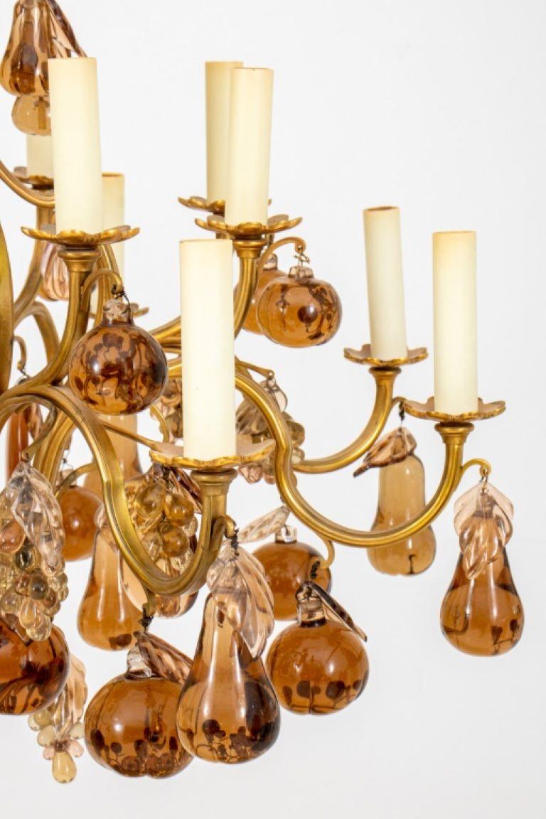 Lustre Louis XV en forme de cage en métal doré à 16 lumières, avec un balustre tripartite en verre ambré entouré de deux niveaux de huit lumières (16 au total). Les bras de bougie sont suspendus à des poires, des raisins, des feuilles et des