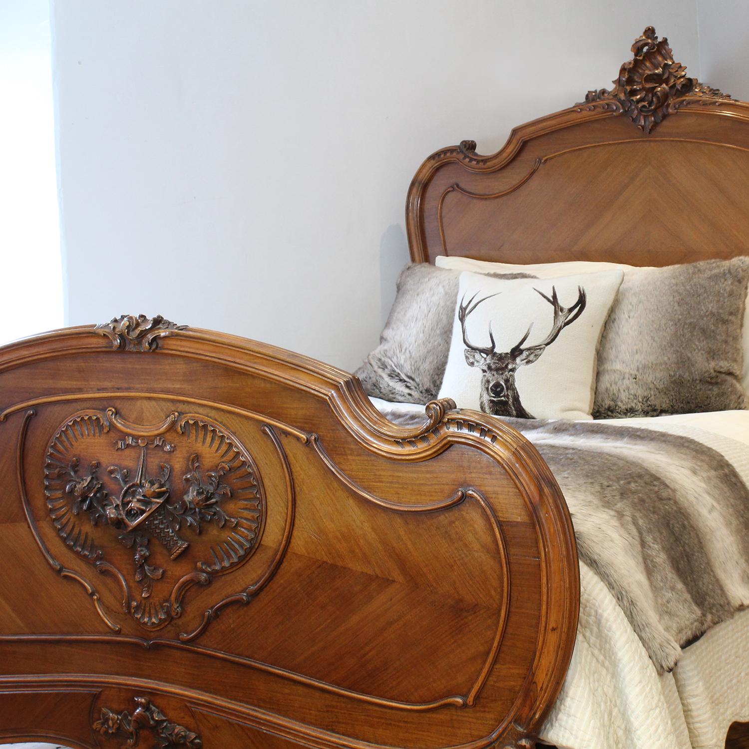 A Louis XV style bed in walnut with shield design feature in the footboard containing a detailed carving of a basket of flowers, and ornate carving on the pediment of the head panel. With elegantly shaped shoulders, quartered veneered panels and