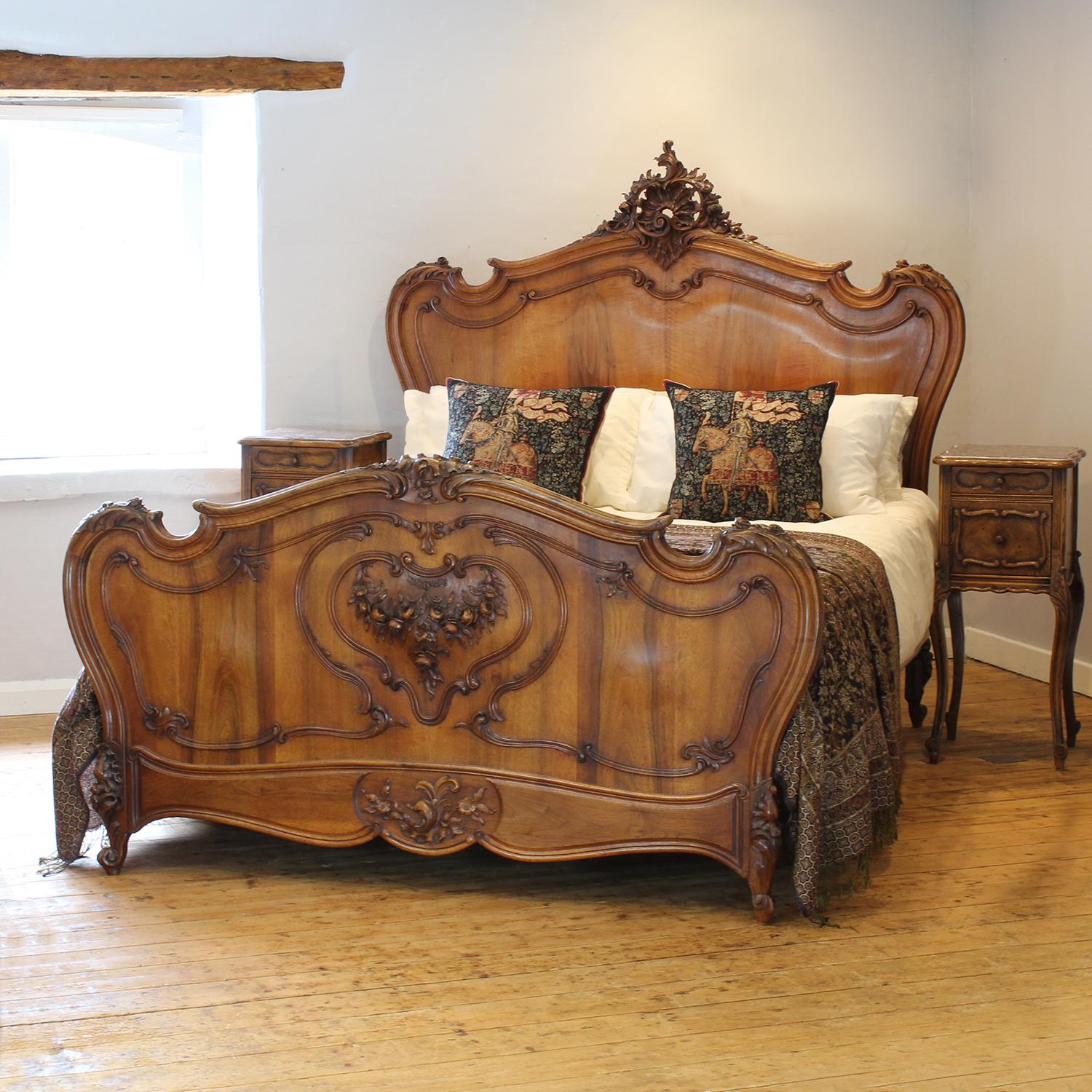 A superb example of a Louis XV style bedstead in solid walnut in a flamboyant rococo design, with pronounced shoulders, decorative beading, ornately carved pediment and central shield carving in foot panel of a garland of roses. The finely grained