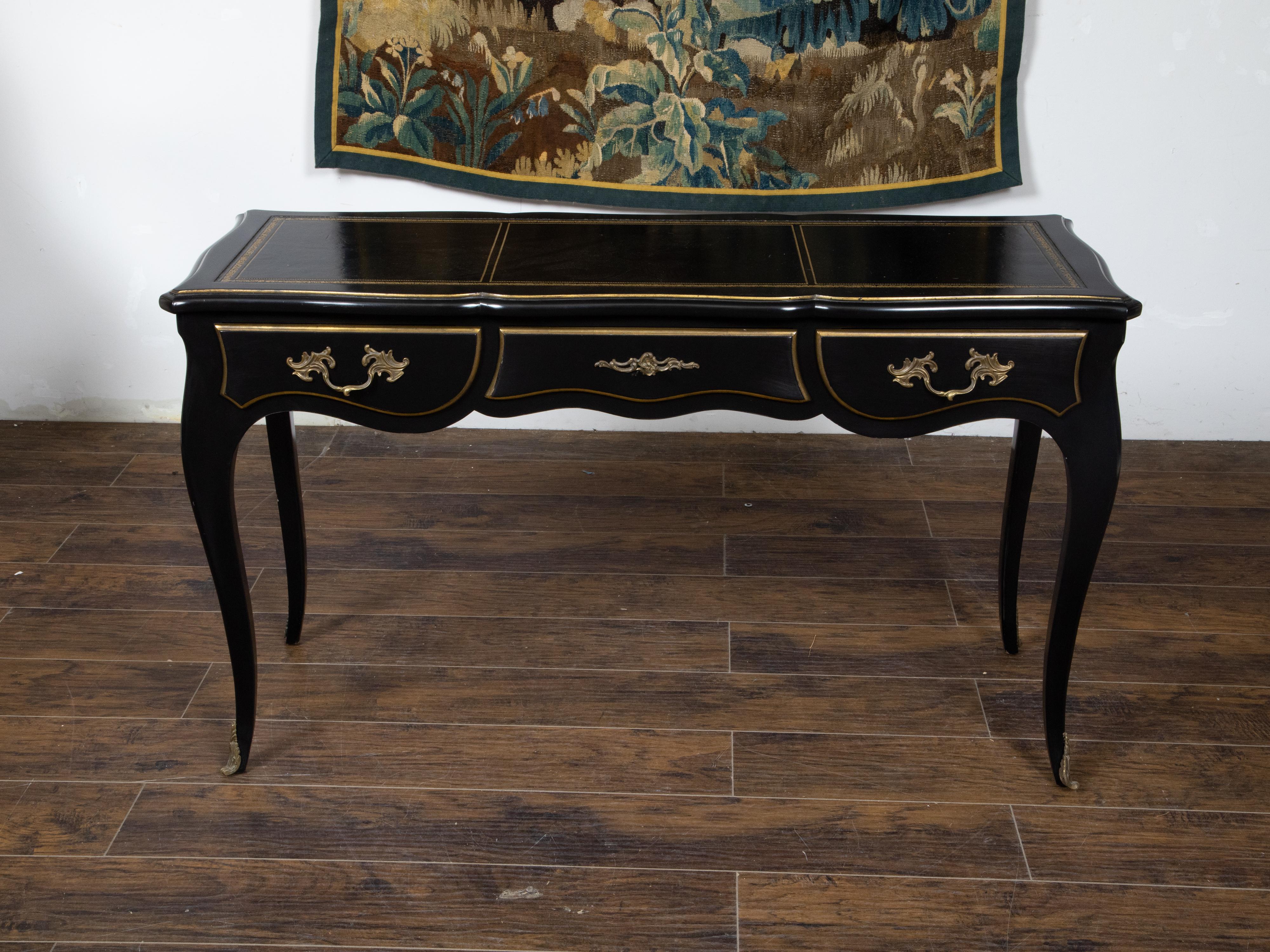 A Louis XV French style black lacquered desk from the mid 20th century by maker Auffray and Co, with leather top, gilt accents, bronze mounts and three drawers. Created during the Midcentury period, this black lacquer desk, made by Auffray and Co