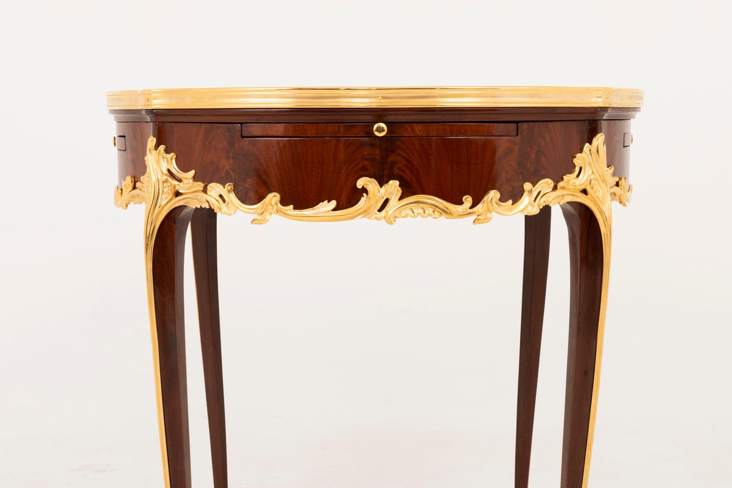 Circular Louis XV style bouillotte table in kingwood marquetry standing on four cabriole legs.
Four apron leaves with a curved frontal edge covered with brown leather hit with gilt irons with a decor of foliage scrolls and opening by a small gilt