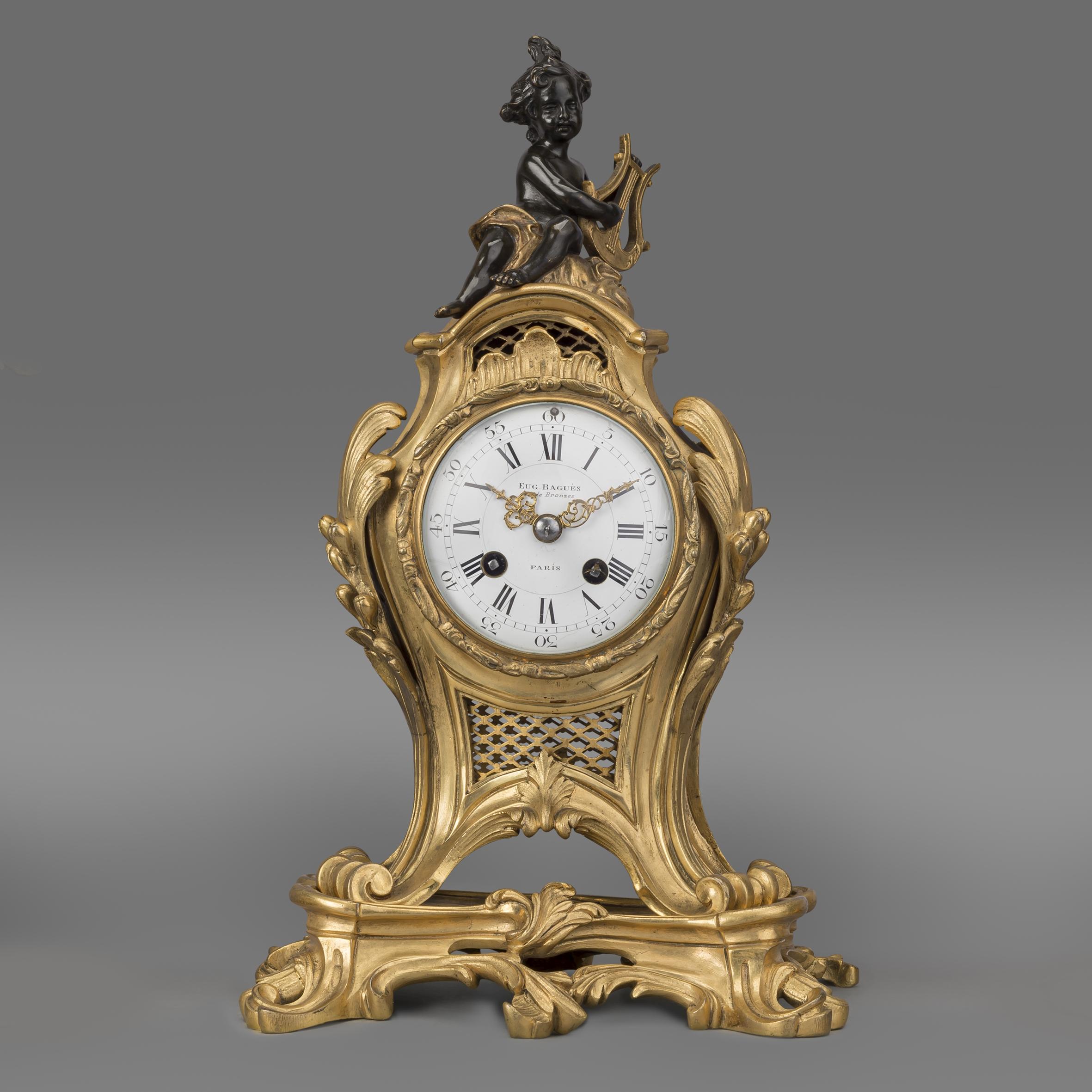 Garniture de pendule figurative de style Louis XV en bronze doré et patiné de la Maison Baguès. 

Ce rare exemple de garniture d'horloge de la Maison Baguès possède un mouvement de huit jours à deux trains sonnant sur une cloche. 

La garniture