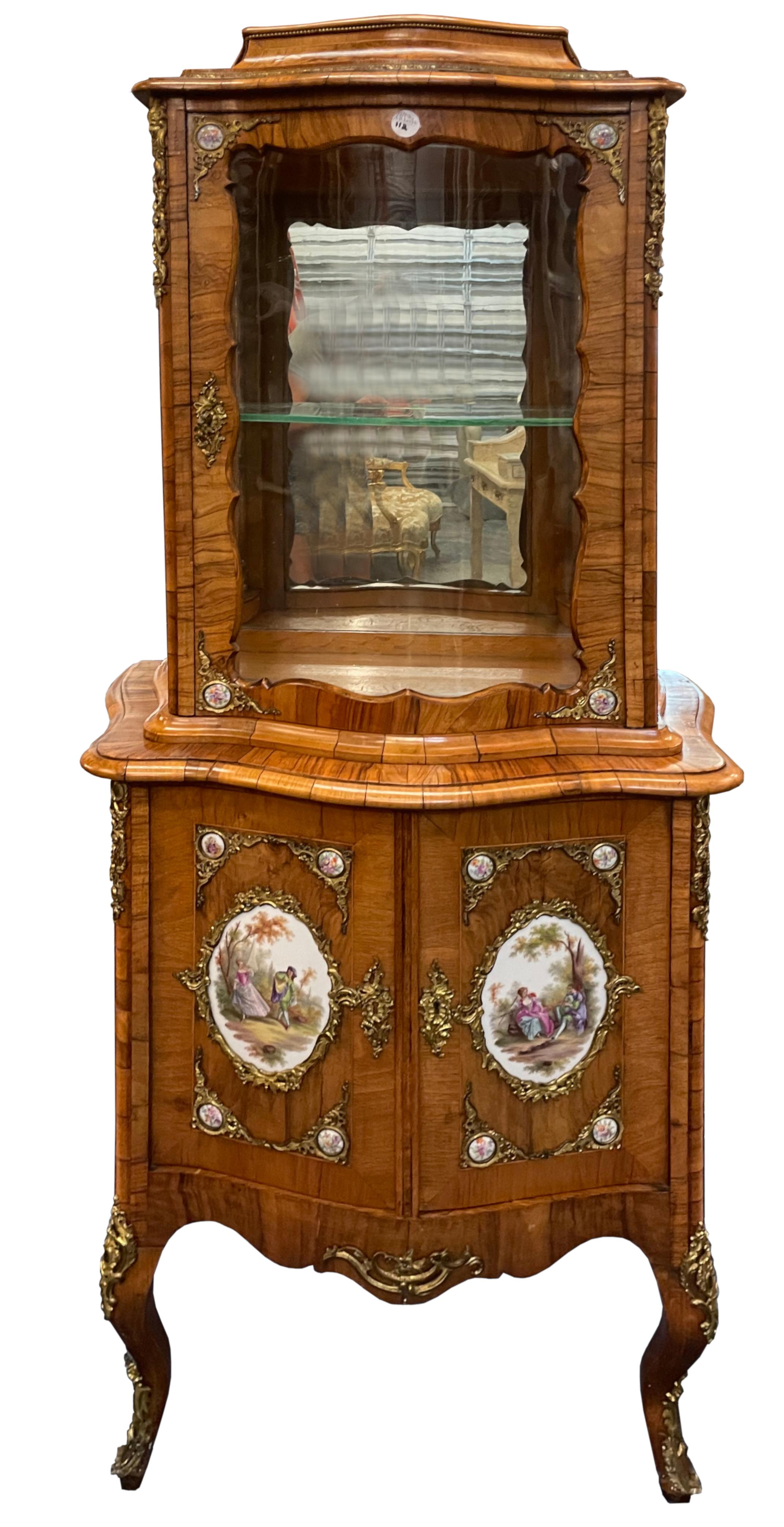 Louis XV Style Bronze & Porcelain-Mounted Walnut Vitrine Cabinet 
The recessed upper part with a nowed glazed door with glazed sides, the lower part with two serpentine-shaped doors, each fitted with a porcelain plaque decorated with an amorous