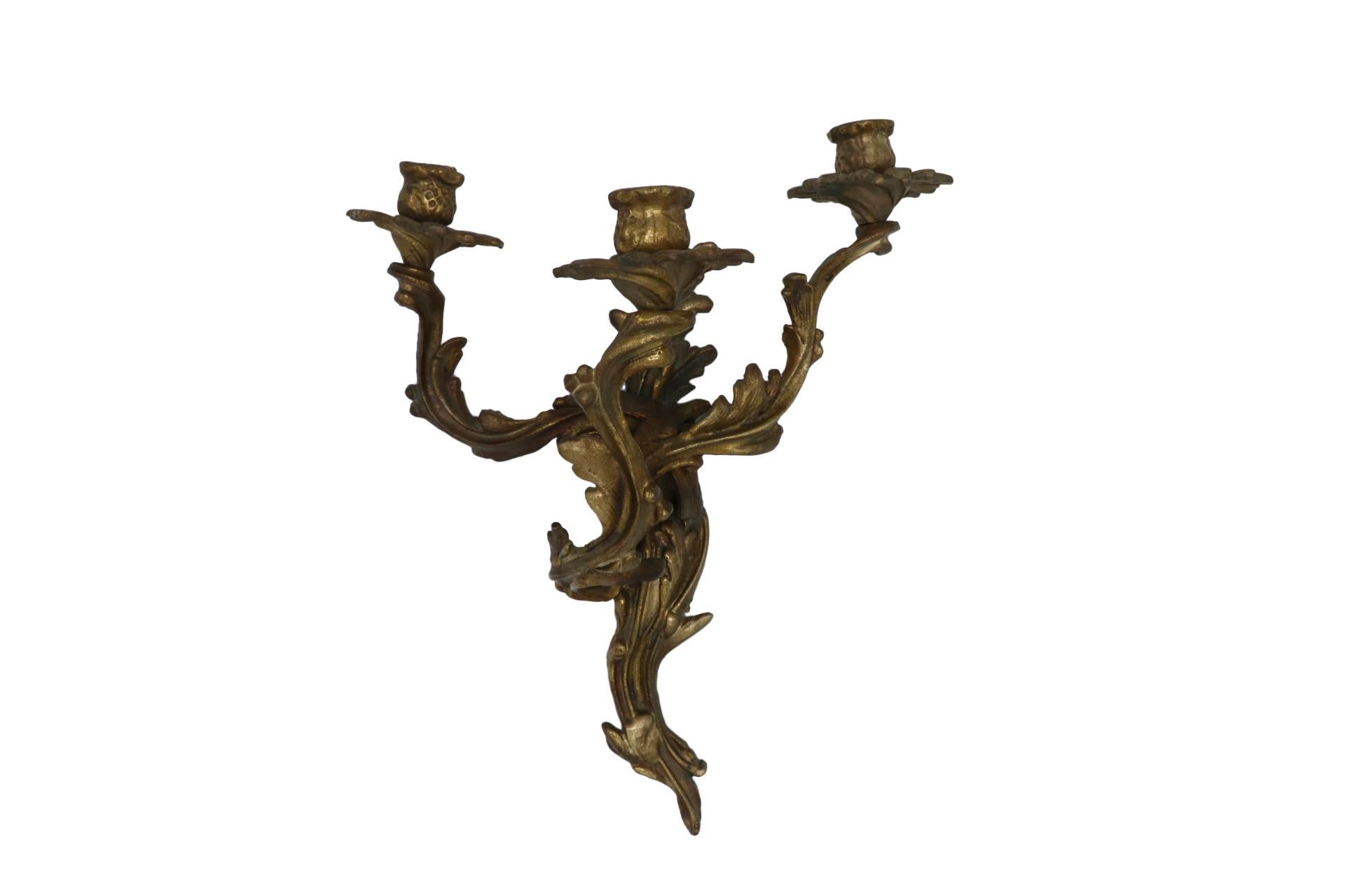 A pair of Louis XV style bronze sconces. Three asymmetric acanthus leaf arms scroll upward supporting floral wax pans and thistle shaped capitals. Dimensions per sconce.