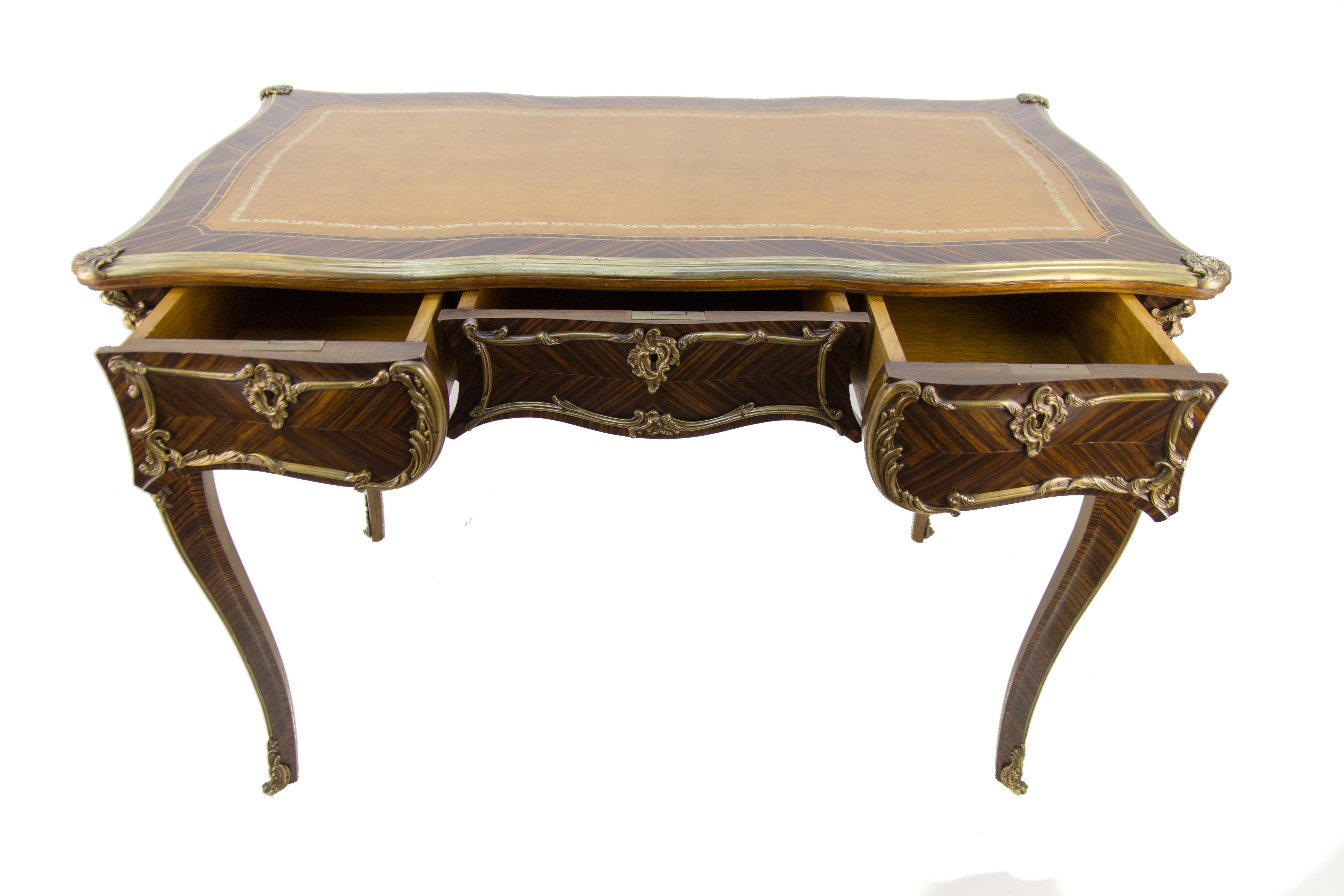 This fine Louis XV-style desk has a leather top framed by bronze borders. The writing desk is raised on cabriole legs headed by floral and leaf cast mounts that have finely finished walnut veneer on all sides. The desk is fitted with three drawers