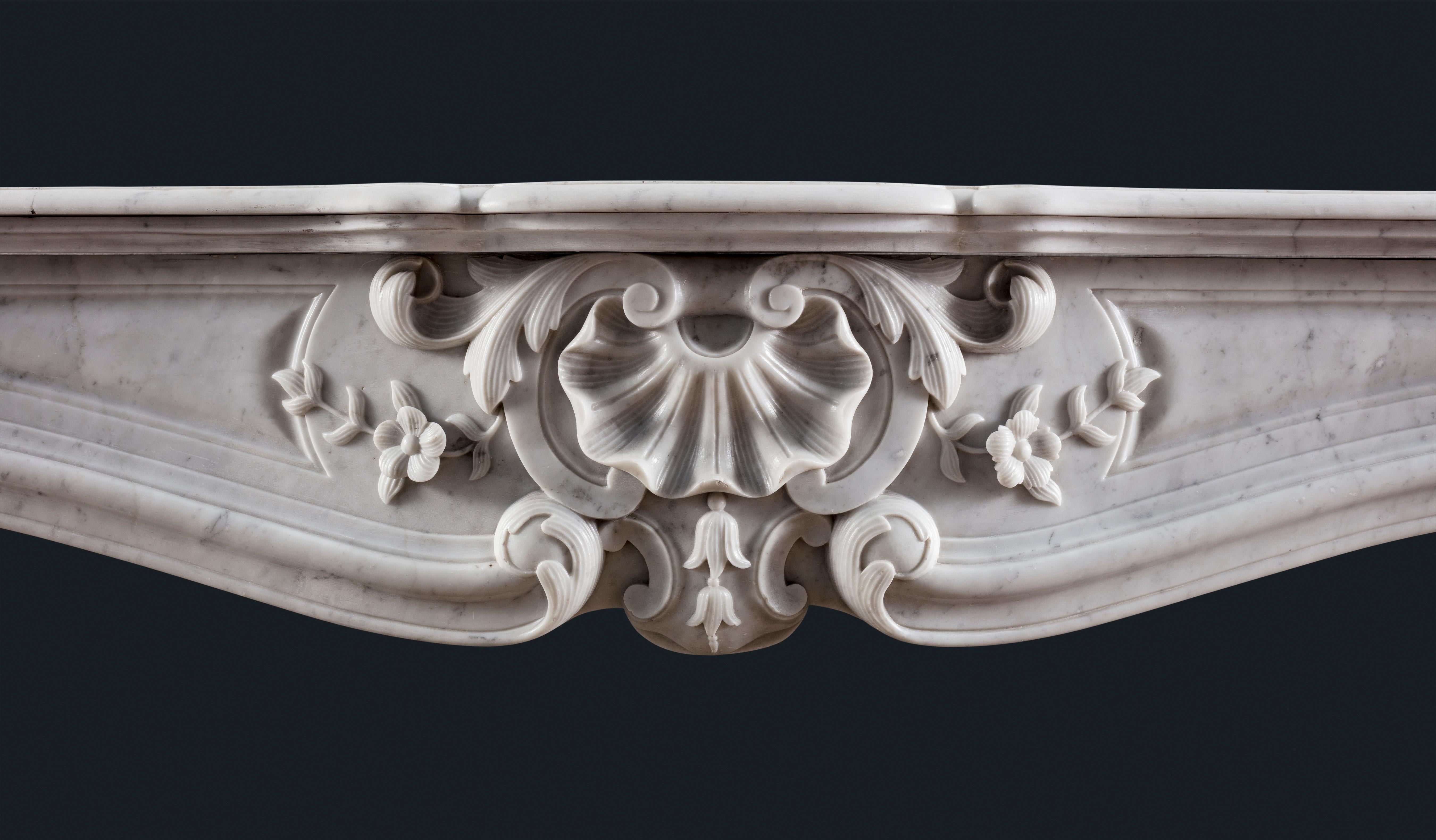 An antique nineteenth-century Louis XV-style Rococo Carrara marble fireplace surround, the elaborately shaped and stepped marble shelf sitting atop a frieze centred by a cartouche composed of scallop shell, campanula flowers and acanthus fronds, the