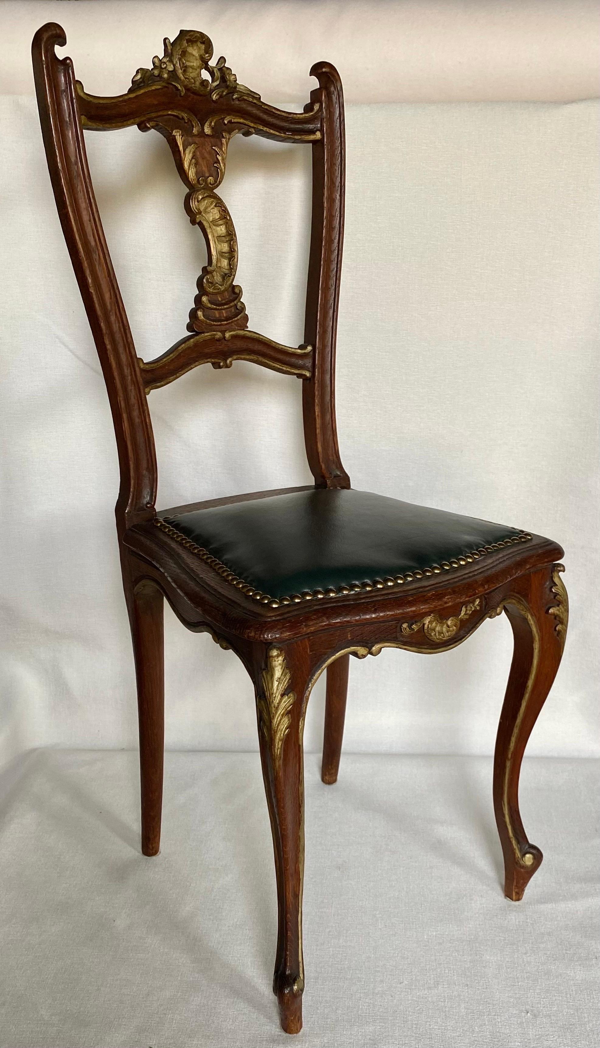 Louis XV style side chair with carved scrolled gilt accents and curved cabriole legs. This highly decorated small accent chair is upholstered in dark green leather and trimmed in brass nail heads. Would make a fabulous desk chair or could be