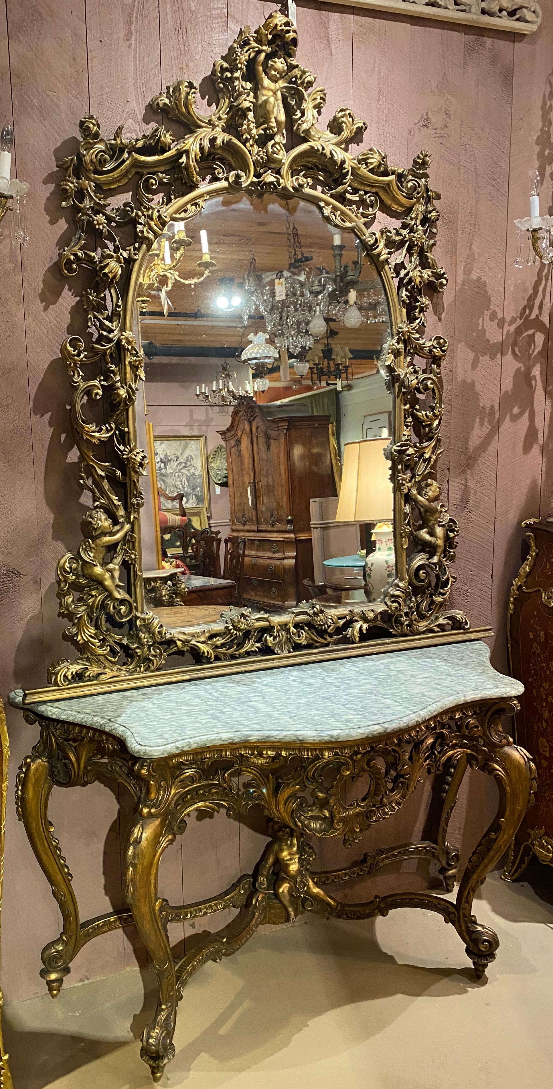 A fabulous Louis XV style carved giltwod console with shaped marble top and arched mirror en suite, adorned with heavily carved and gessoed cherub, foliate, and scrollwork decoration, with cabriole legs and cherub decorated stretcher. Dates to the