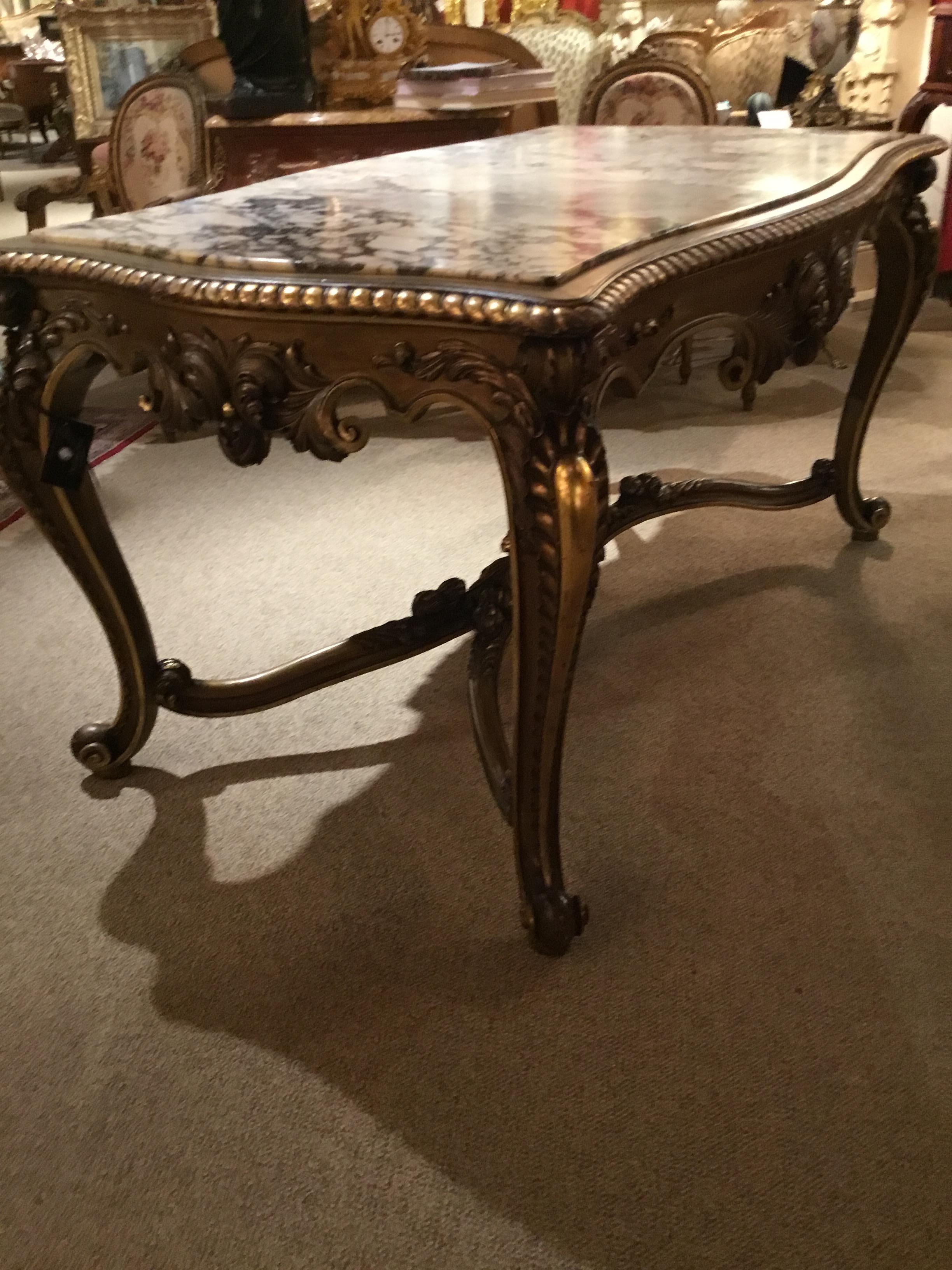 Center table in antique gilt wood with deep carving and a centered foliate scroll design across the front
Frieze and a bold curved leg with scallops down each leg. The elegant stretcher is curved and joins 
At the center with two embracing angels