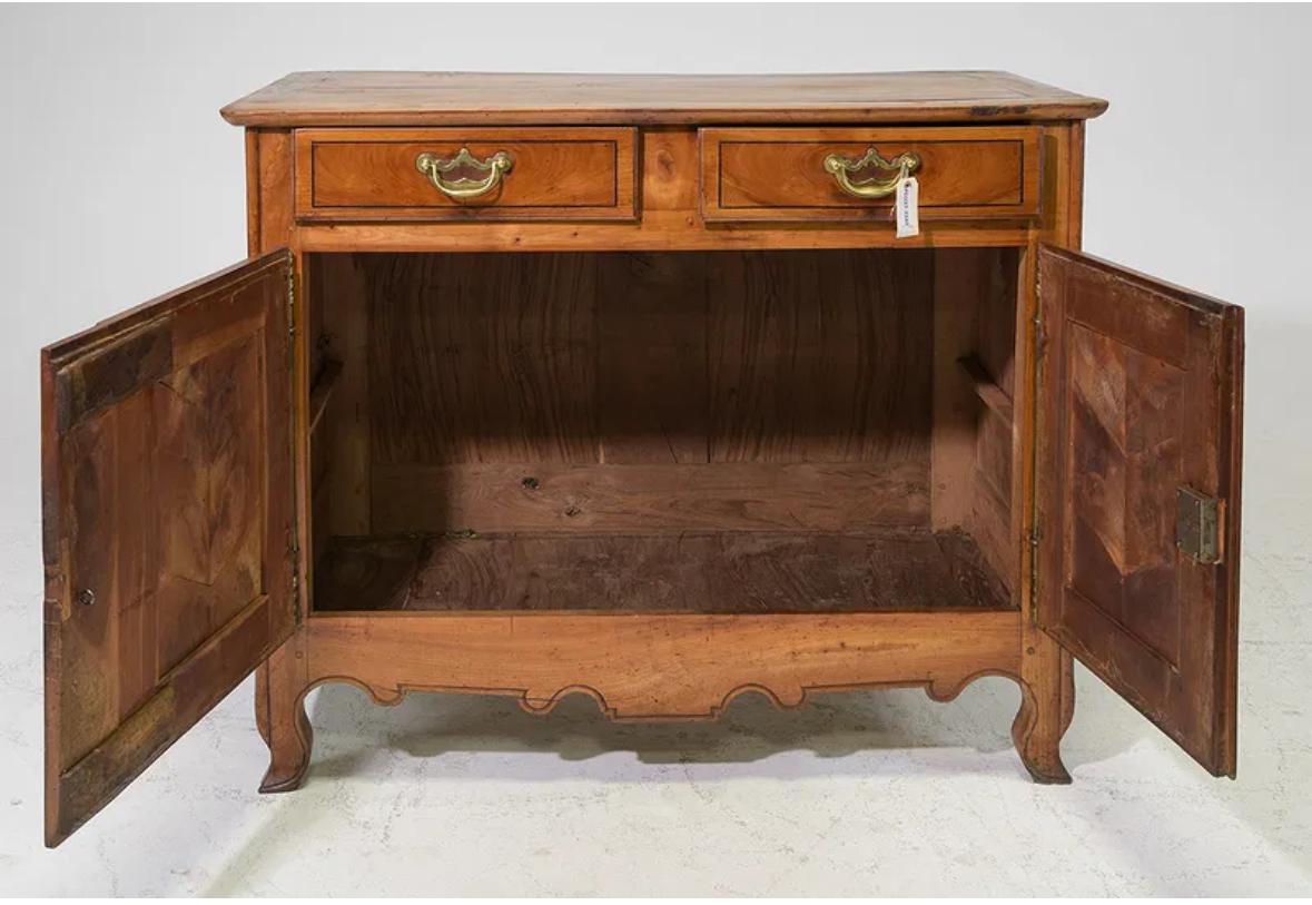 Dieses Möbelstück im französischen Landhausstil verfügt über eine rechteckige Platte mit abgerundeten Kanten, zwei obere Schubladen und getäfelte Seiten. Er zeichnet sich durch verschnörkelte Stahlschilder und -griffe, kurze Cabriole-Beine und eine