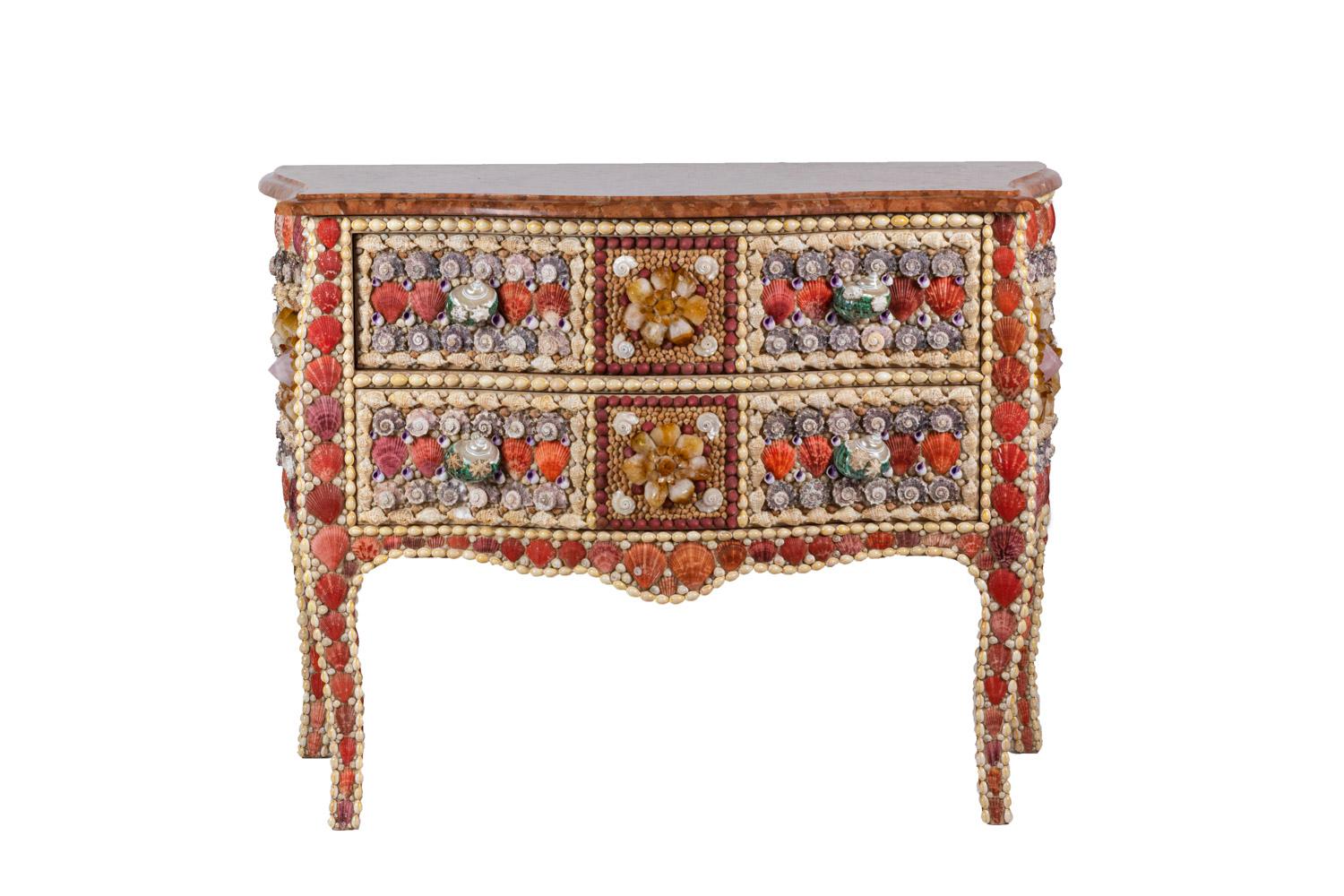 Louis XV style commode opening by two front drawers on two levels without crossbar and standing on four cabriole legs. Bulged shape and scalloped inferior crossbar.
Front and sides decor of shells and quartz, in orange, red, purple and cream tones.