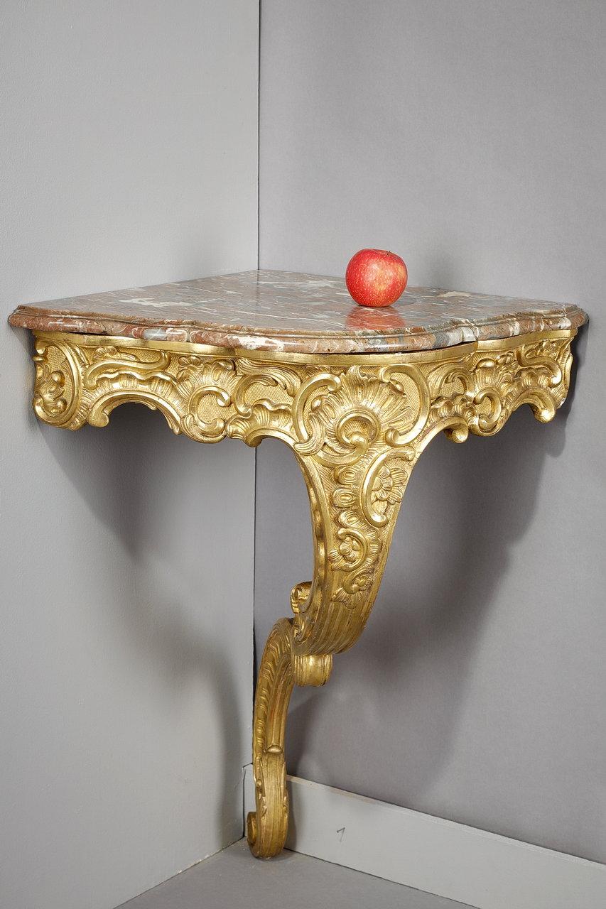 Louis XV style corner console in carved, molded and gilded wood. A rich decoration of foliage and volutes on a lozenge background forms the foot of this console table. The top of the table is made of molded and curved breccia marble. The design of