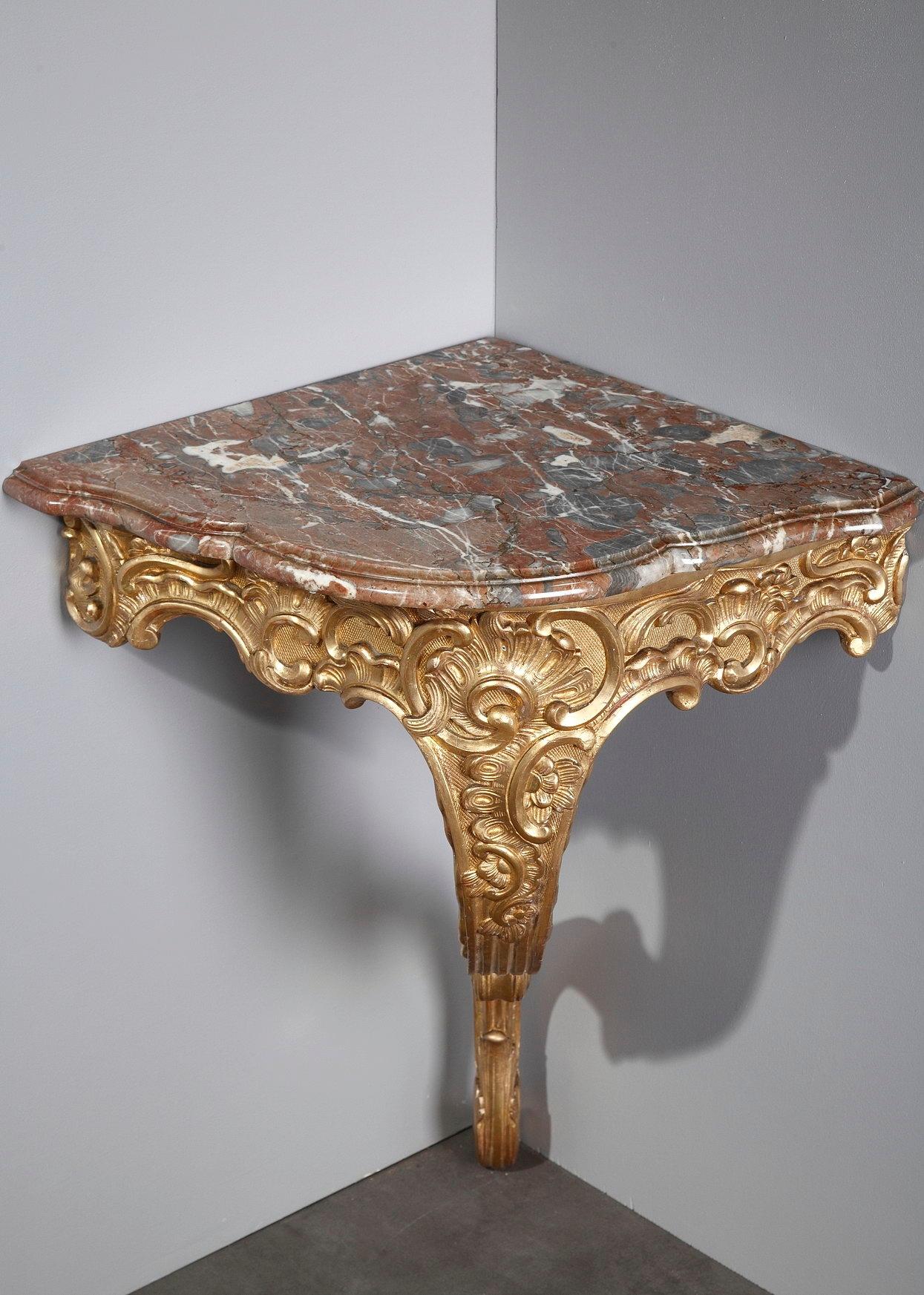 Two Rococo style giltwood corner consoles, carved with naturalistic, voluptuous flowing foliage and scrolls. The console table reached the height of fashion in France during the Louis XV period. The design of the foot and the belt alternates curves