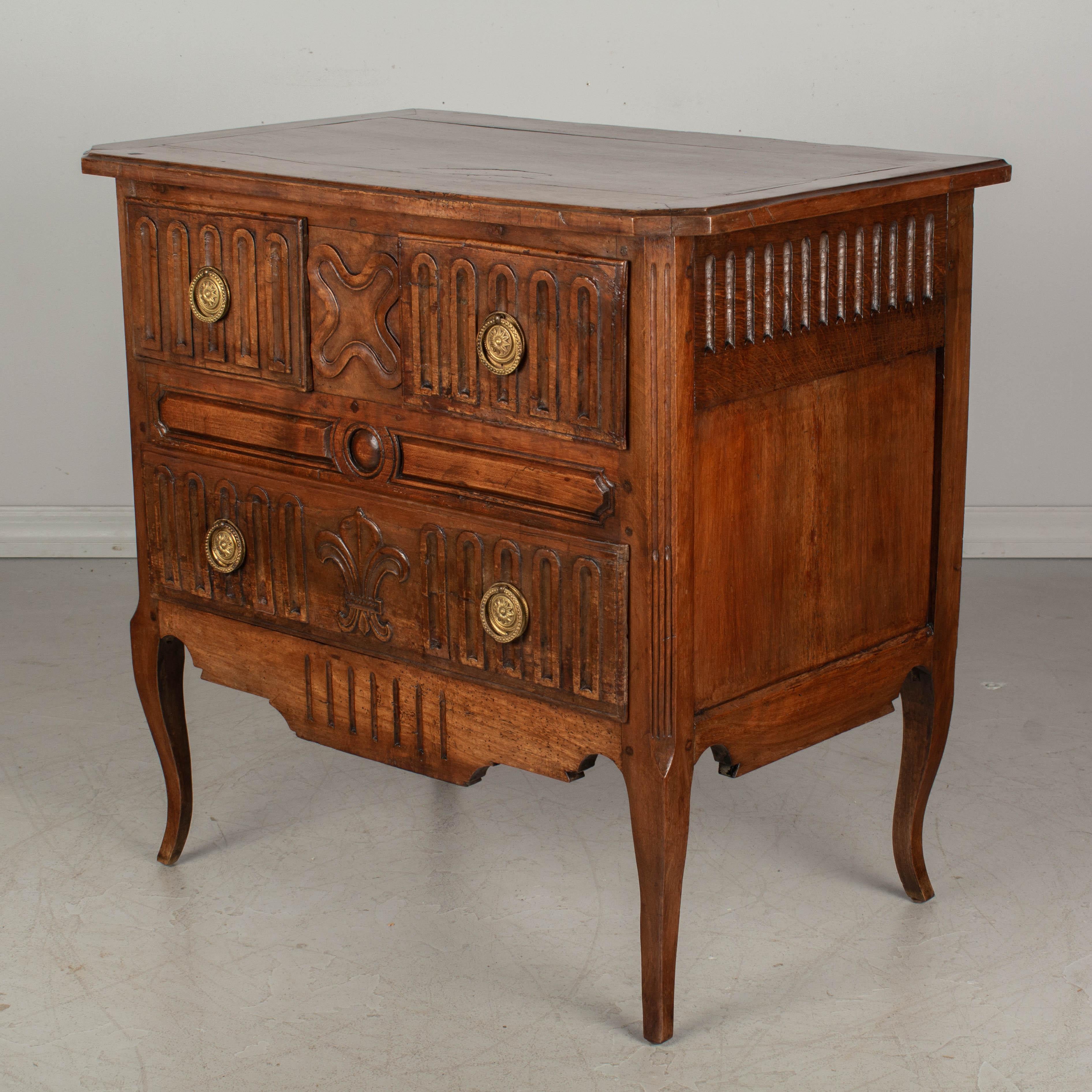 A Country French commode, or chest of drawers, made of solid walnut, cherry and fruitwood. Three dovetailed drawers with brass ring pulls. Hand carved decoration including a large Fleur de Lis on the bottom drawer. Beautiful quality to the wood with