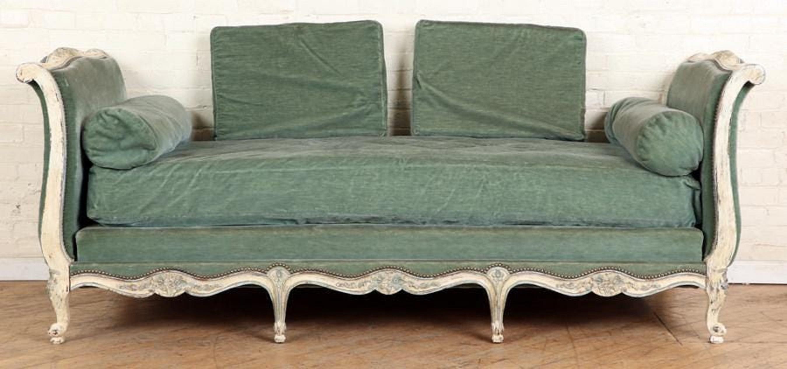 A Louis XV style sleigh-form day bed, the frame carved with flowers and other decoration, in distressed white and blue painted finish with blue/green vintage mohair upholstery and cushions.
