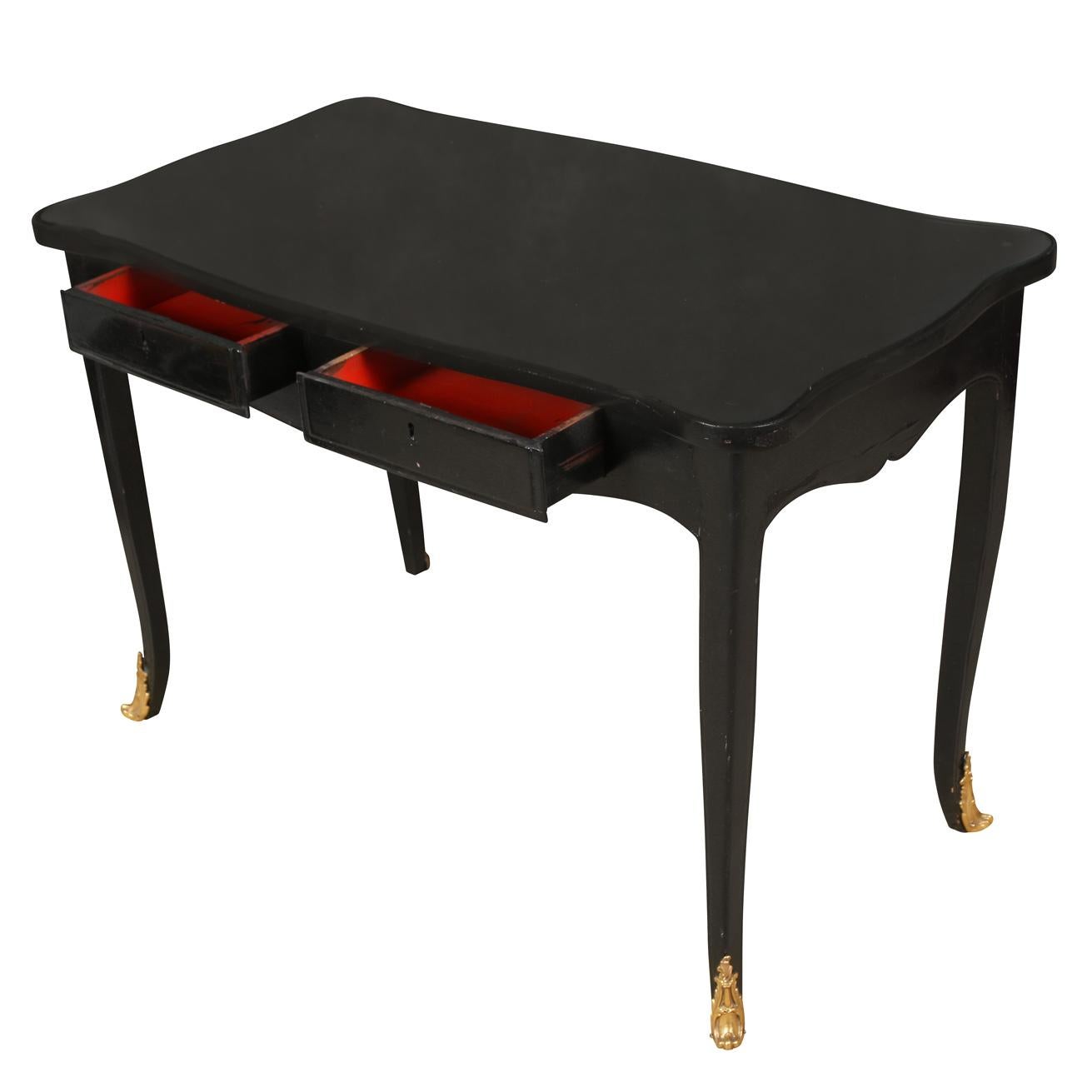 An ebonized writing desk in Louis XV style with cabriole legs and ormolu mounts to the feet, two drawers, a curved apron and a glass top.