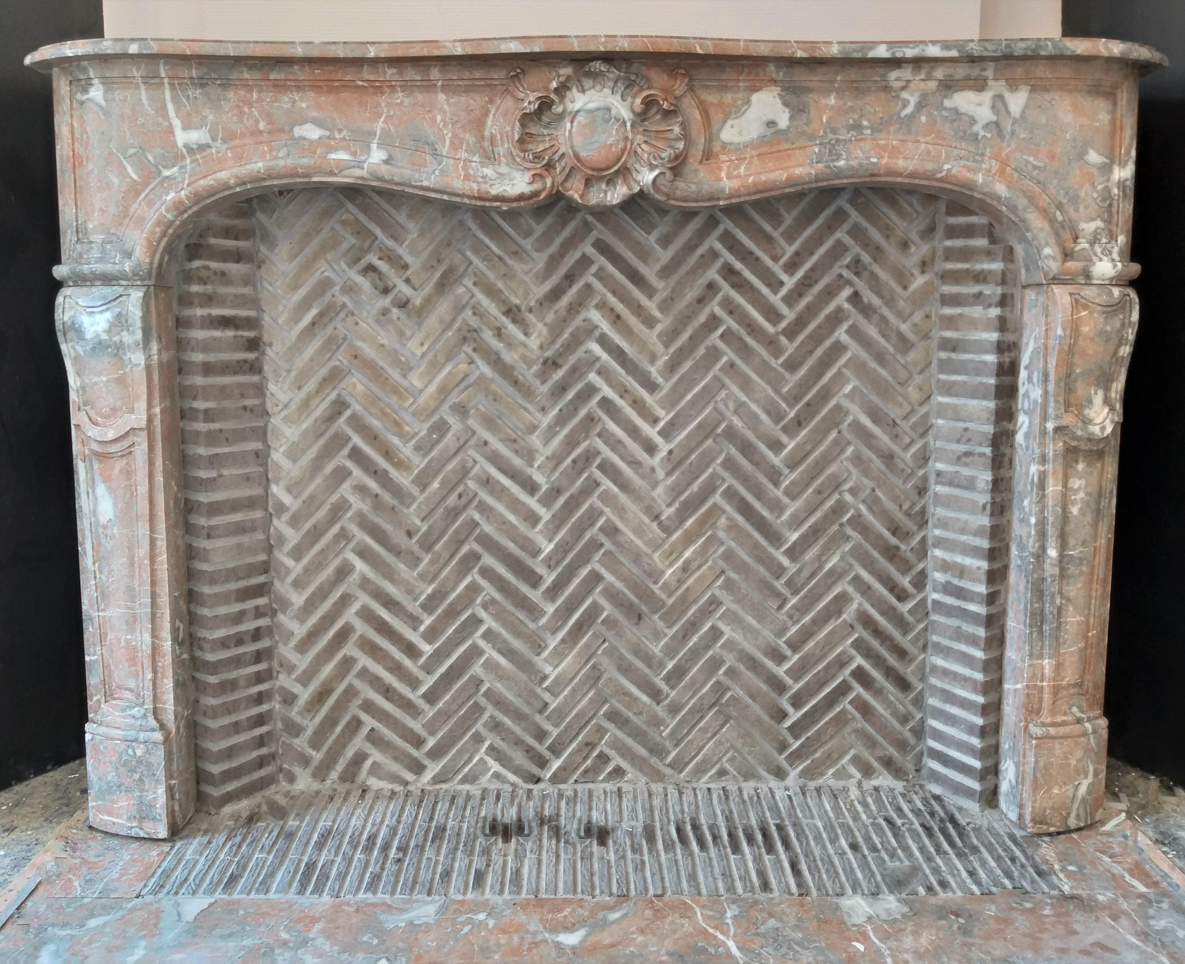 This charming, antique Louis XV-style fireplace was made out of the most beloved Belgian red marble: Saint Rémy, during the 19th century.
The colors of Saint Rémy are soft-toned red, grey and white veins. The center of the slightly curved frieze is